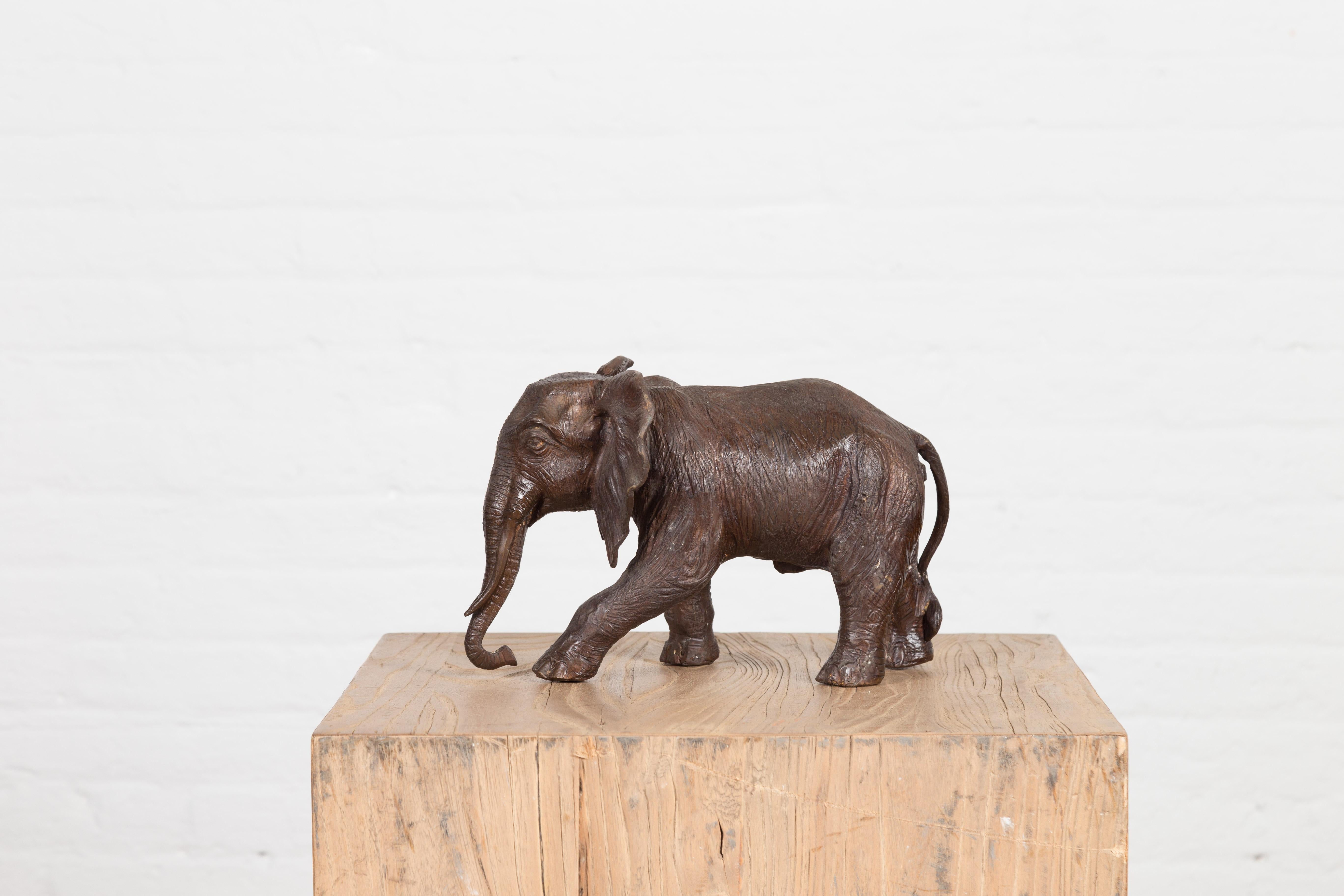 A lost wax cast bronze sculpture depicting a walking baby elephant in dark patina. Created with the traditional technique of the lost-wax (à la cire perdue) which allows for great precision and finesse in the details, this bronze statue depicts a