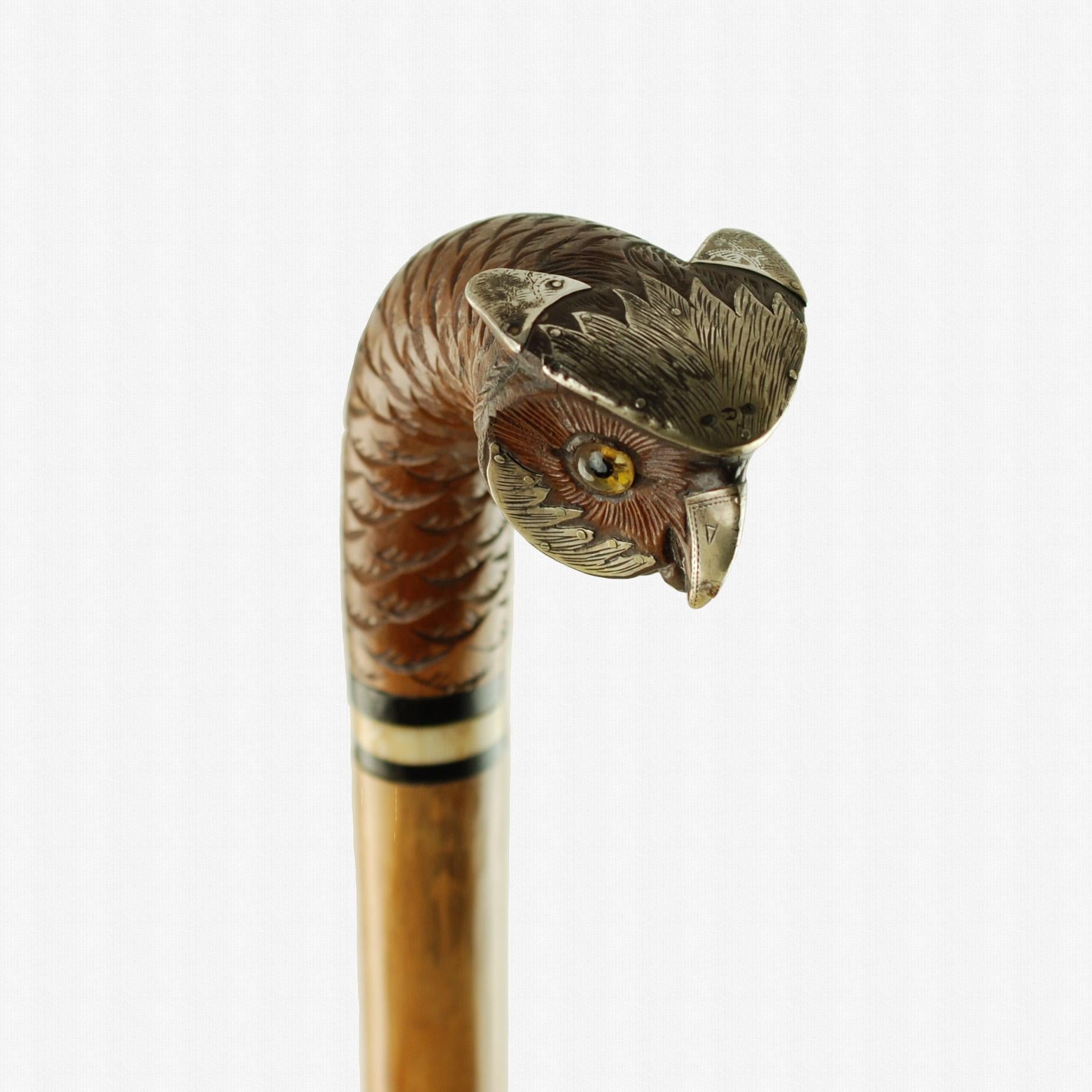 Cette fabuleuse canne antique présente une poignée en forme de tête de hibou sculptée à la main, accentuée par des montures en argent autrichien et des yeux en verre. Le manche en bois figuré est orné d'un plumage texturé et présente une finition