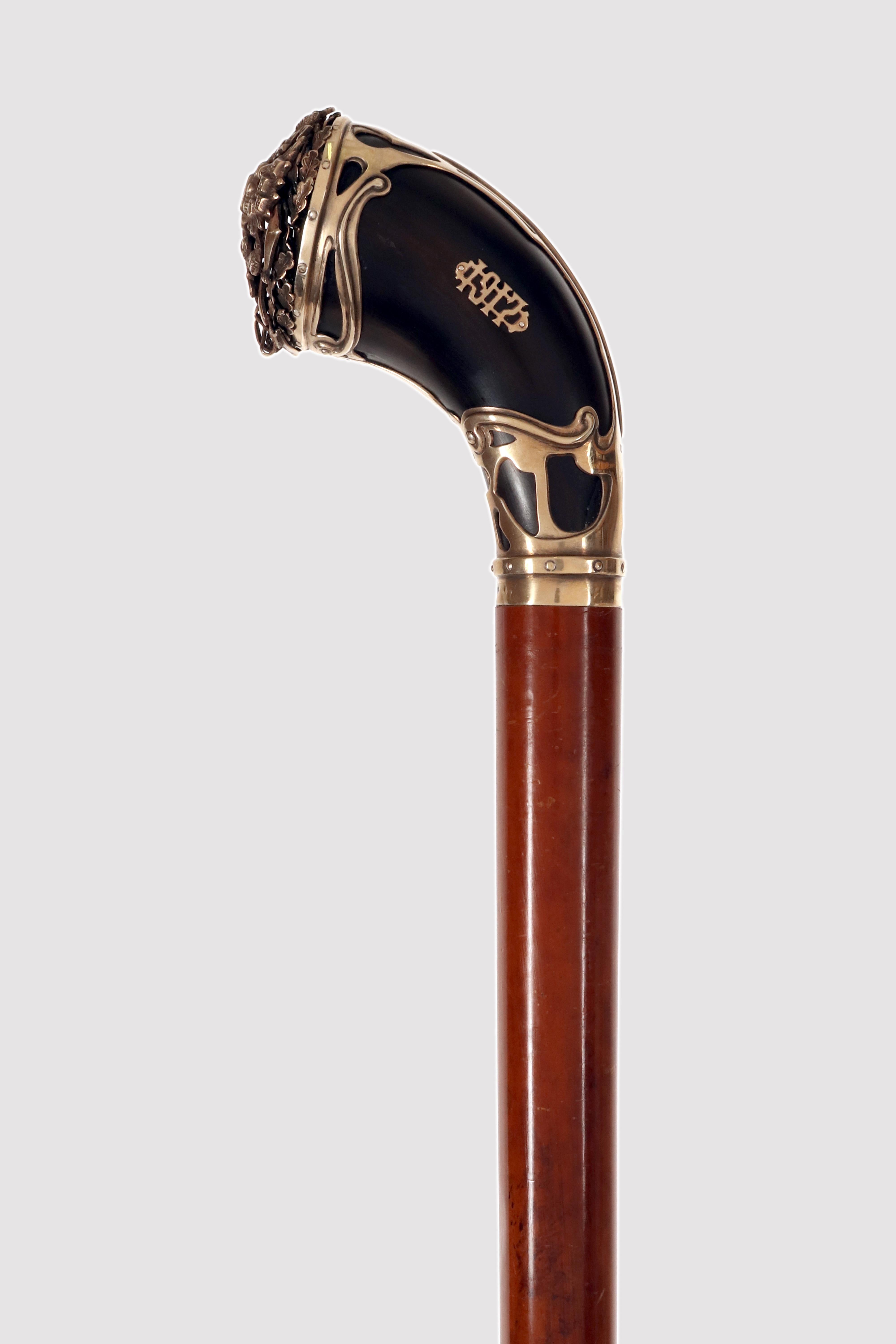 Bastón con caña de madera de Malaca y pomo de cuerno de buey con bandas y casquillo de plata dorada que representa un águila bicéfala.El pomo es de cuerno de buey negro enriquecido con una decoración de plata. La banda es lisa, rematada por un