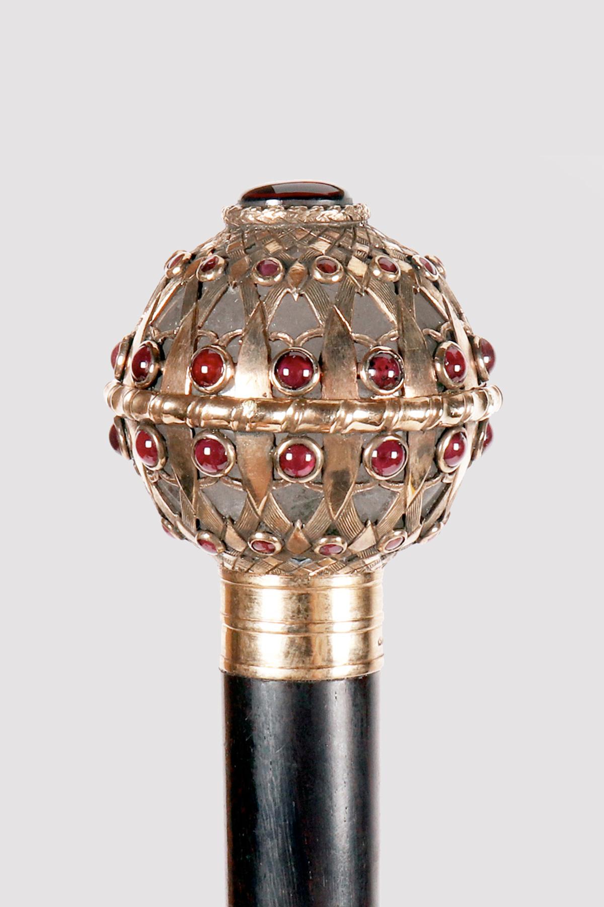 Canne : canne bijou, pommeau en cristal de roche, de forme sphérique, encagé par des bandes entrelacées en argent doré avec cabochons de grenat.  Arbre en bois de serpent. Métal et virole en fer. Signé Leopold van Strydonck(1865-1939), orfèvre et