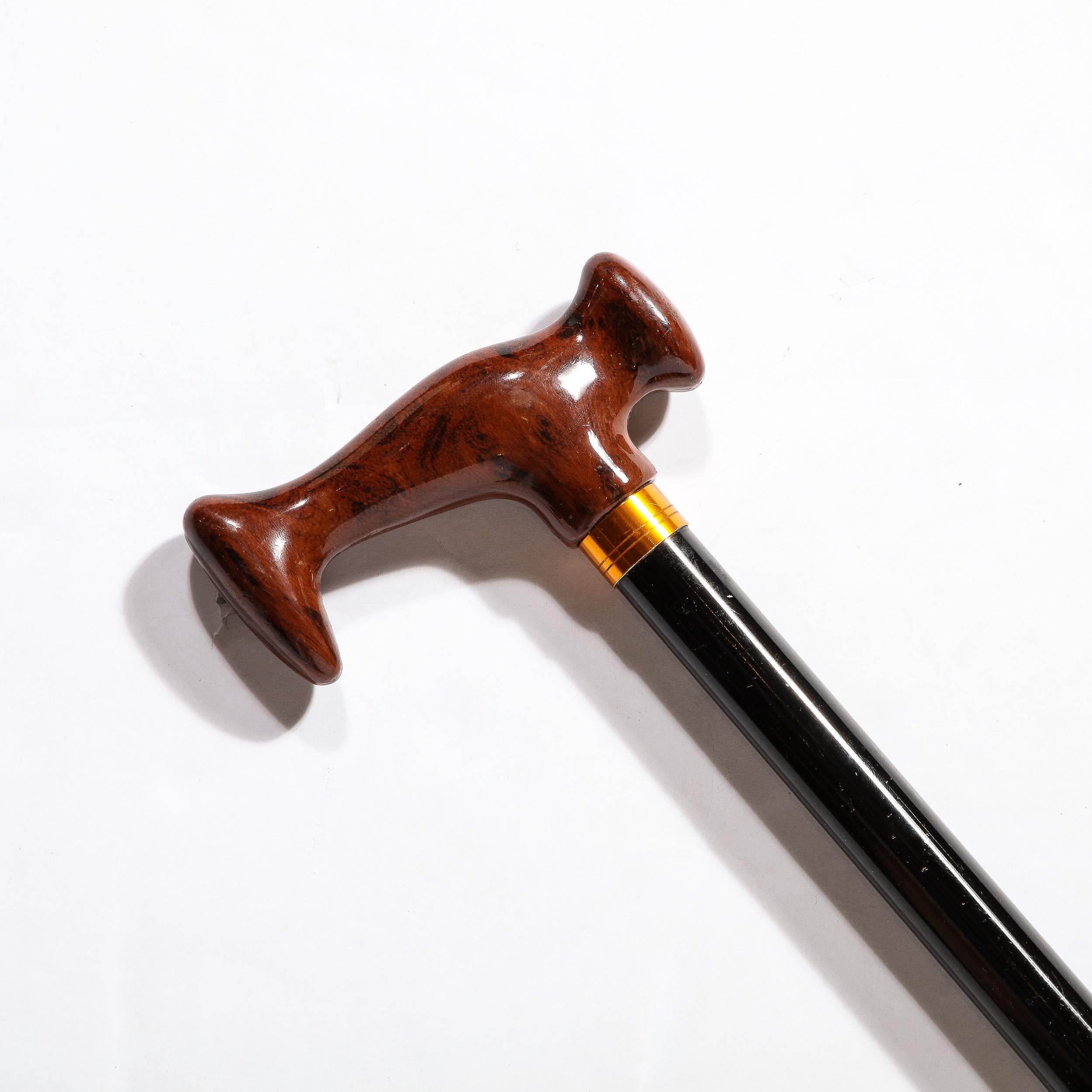 This Walking Stick in Faux Walnut and black enamel originates from the United States during the 20th Century. Features a lovely sculptural handle in faux walnut, leading to a brass fitting at the neck above the black enameled body. The height can be