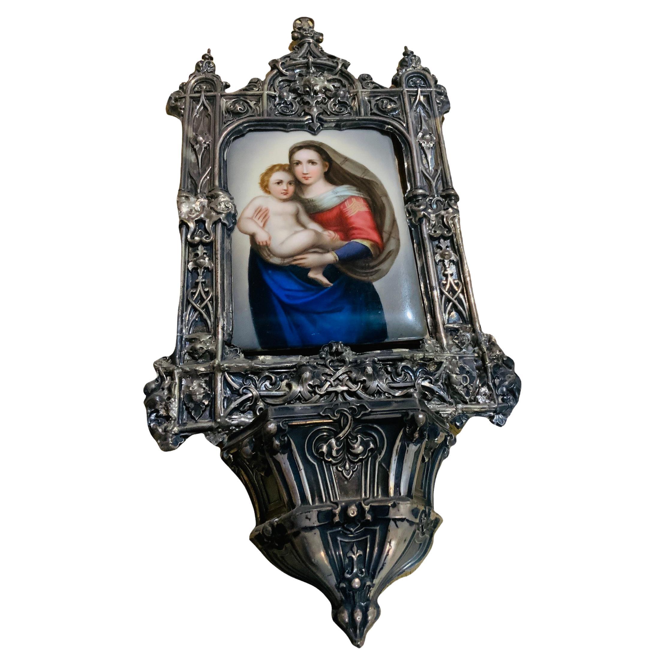 This is a hand painted KPM style rectangular plaque of the Sistine Madonna framed in a wall brass holy water font. The brass frame depicts three arcs, two small semicircular in the sides and a large ogee in the center. All of them decorated with
