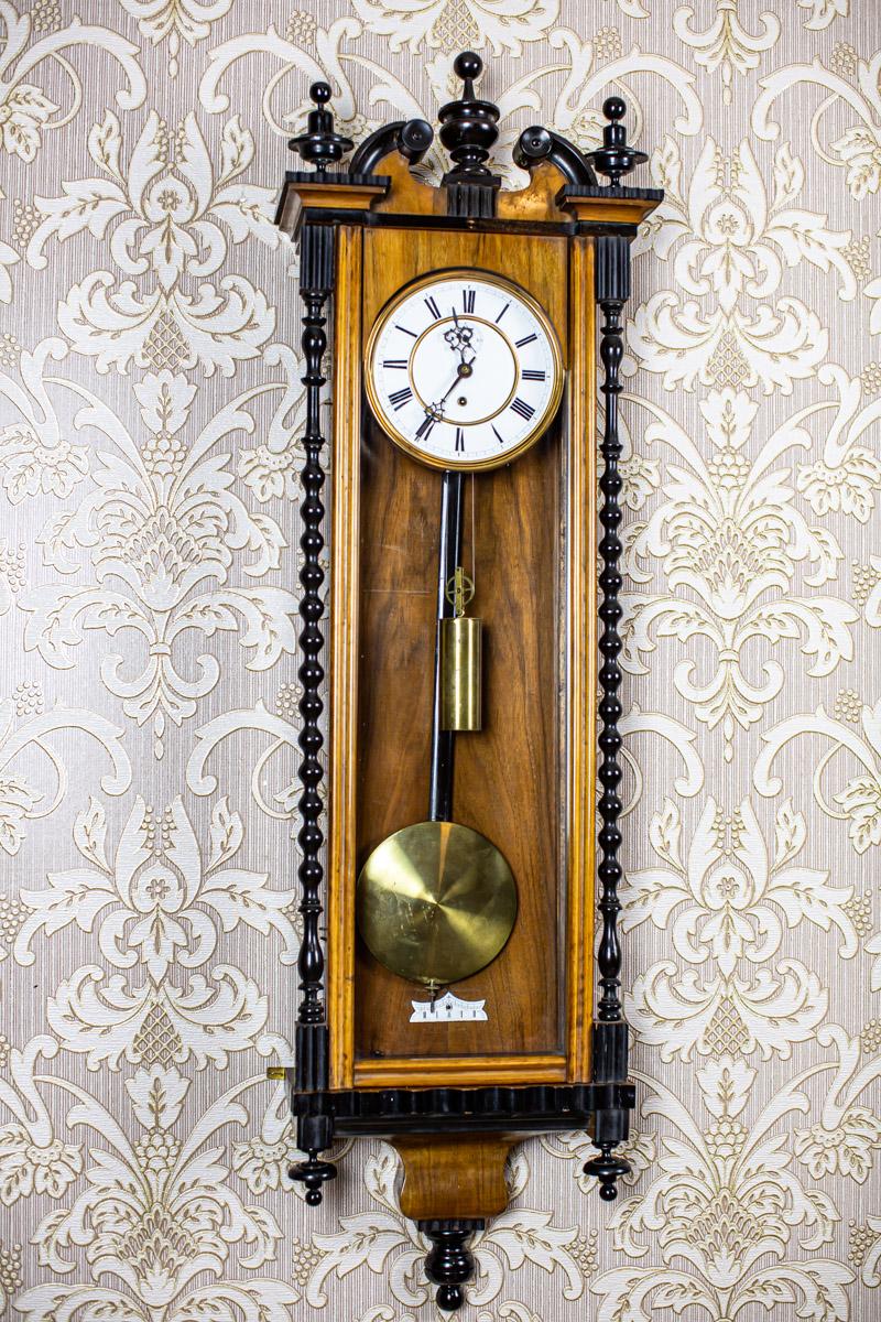 We present you a wall clock from the late 19th with a weight on chain as the power source.
The case is topped with an irregular crest and finials.
They are known as Vienna regulators and were made in the Black Forest of Germany. Originally they were