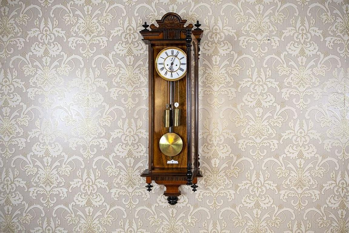Wall Clock From the Late 19th Century in Walnut Case

We present you this wall clock from the late 19th century in a glazed walnut case.
The clock face is porcelain, whereas both the pendulum and weights are made of brass.
Furthermore, the clock