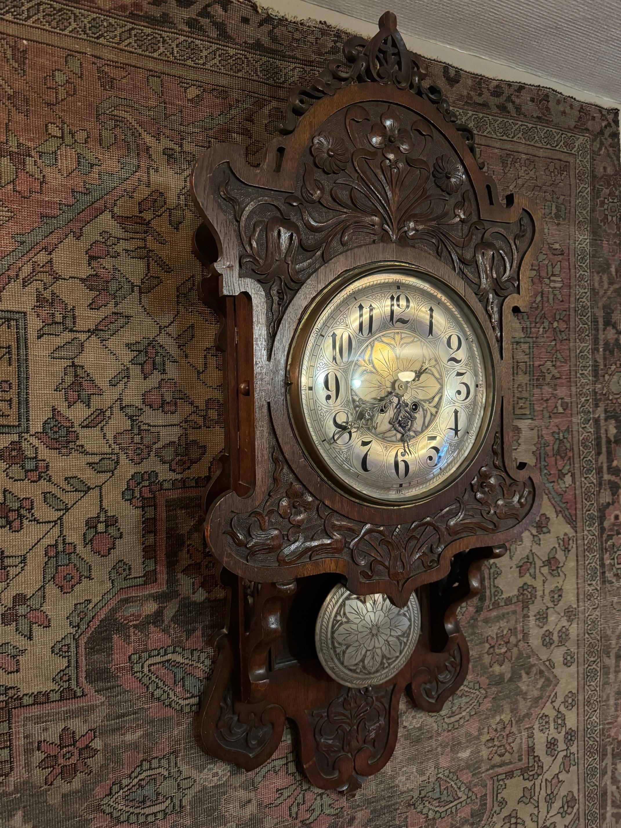 Wanduhr oder Kartell, aus geschnitztem Holz, mit Ranken und Blumen, wahrscheinlich Edelweiß, auf dem Zifferblatt, dem Pendel und den Zeigern, alle drei aus Zinn. 
Sehr schöne Arbeit, dekorativ, Jugendstil deutsch, wahrscheinlich bayerisch. 
Das Holz