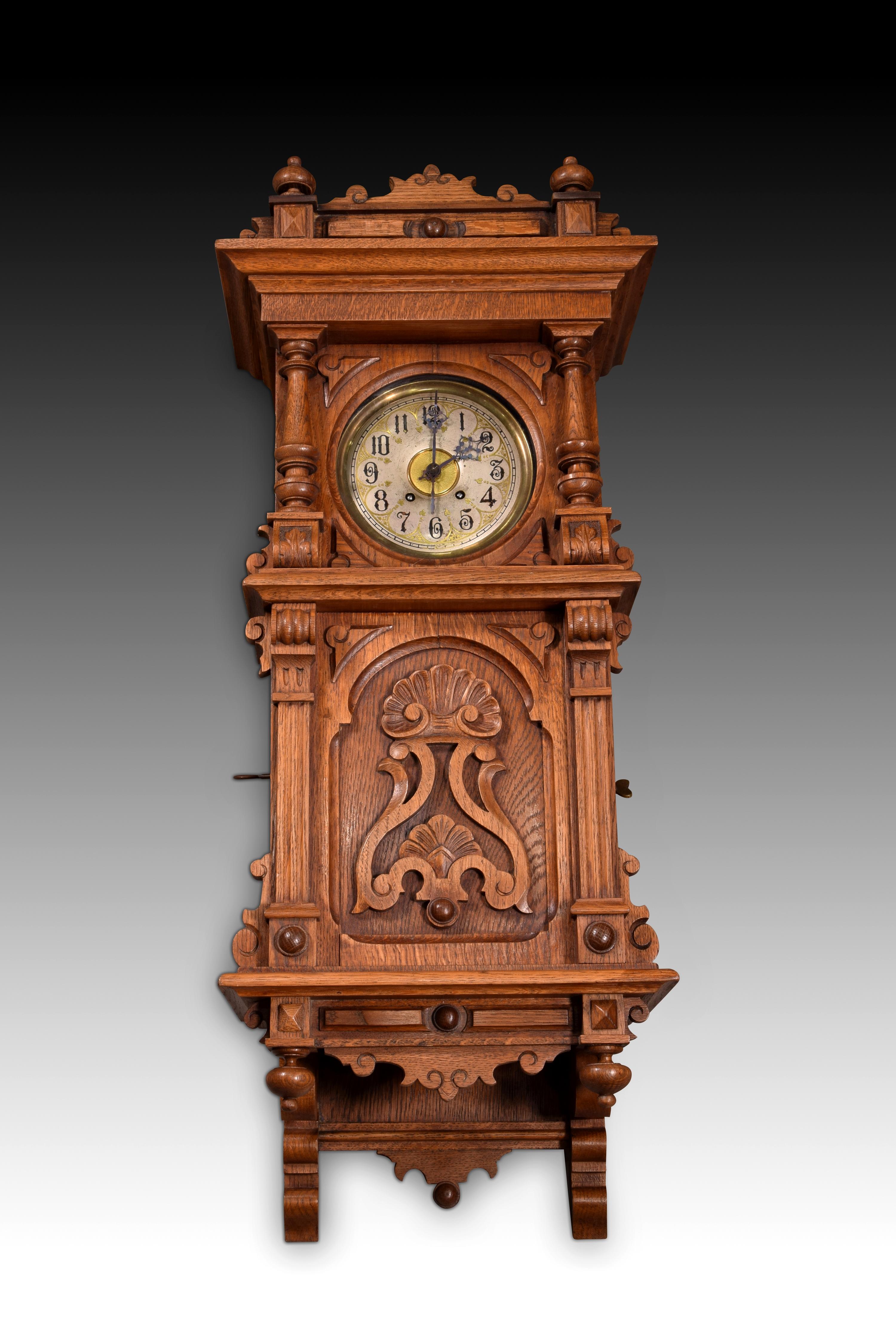 Carved wooden wall clock with metal disc music box, 19th century. 
Clock divided into two parts: the upper part, flanked by columns on mouldings, has a dial with Roman numerals and a chromatic play in silver and gold with engraved details