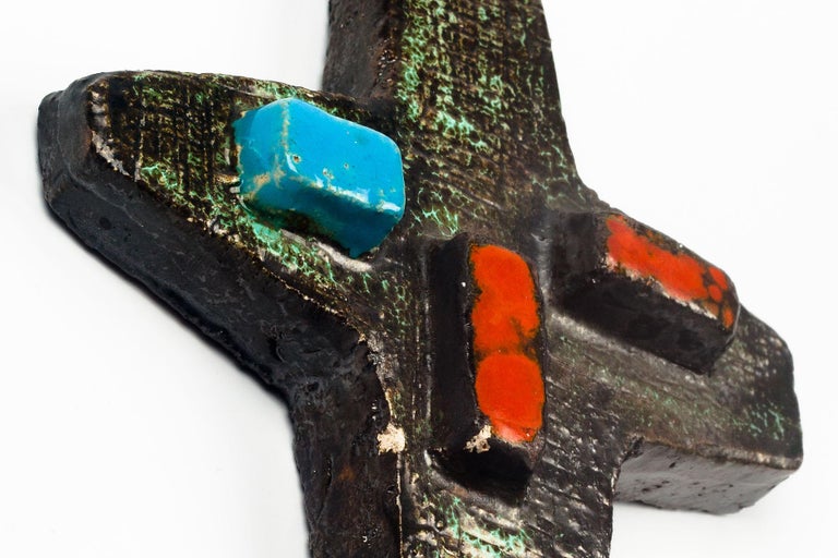 Large crucifix in matte textured and glazed ceramic, handmade made in Belgium in the 1970s. Glazed cross in dark and light green, brown, with red and blue rectangular protrusions. 

This piece is part of a large ceramic crucifix collection, all