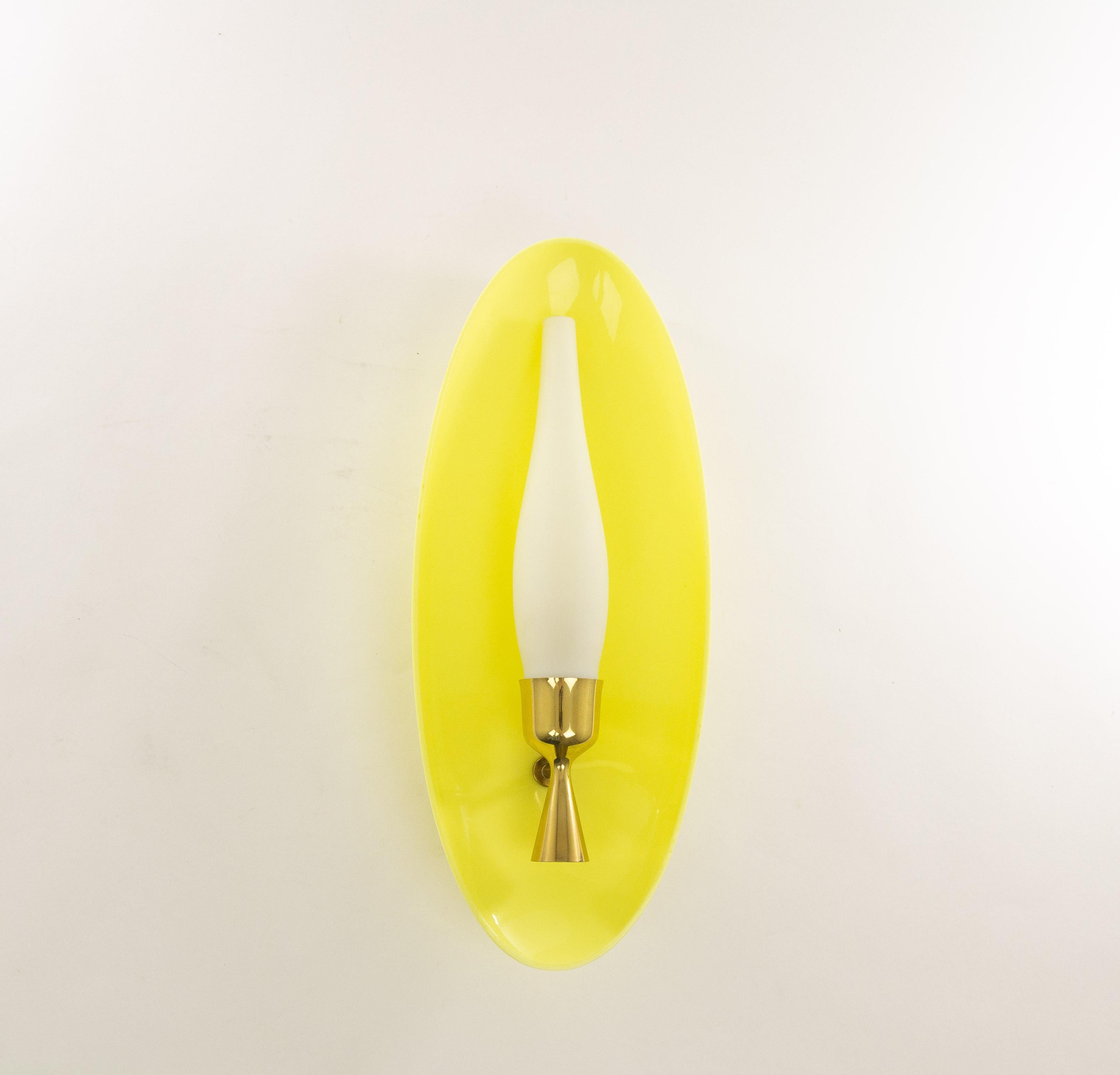 Wall fixture, No. 12645, designed by Angelo Lelii and produced by Arredoluce in 1957.

This wall lamp consists of a striking yellow plexiglas reflector in combination with a duplex white opal candle-shaped glass shade in a brass holder.

The