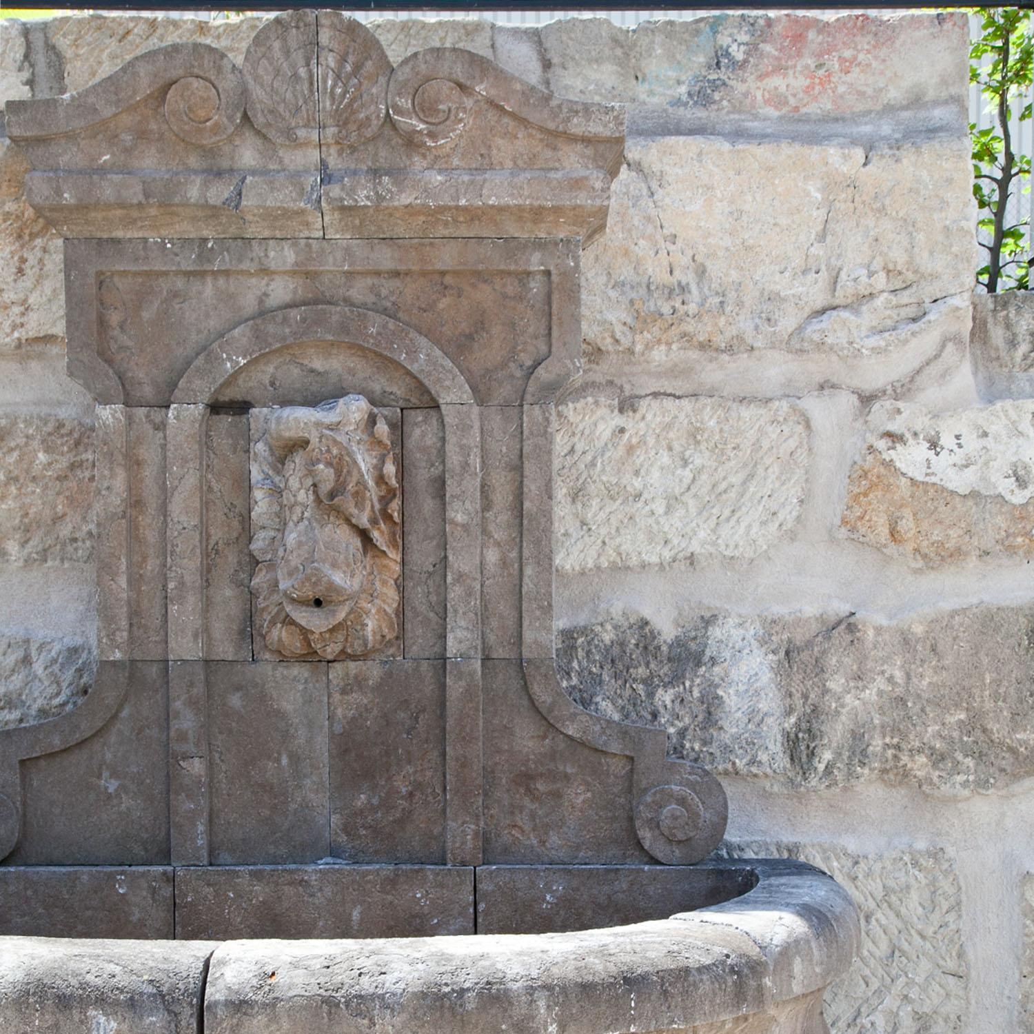 Bluestone wall fountain with a rounded basin and a profiled wall (H: 76 cm). The rear wall with a hand-carved fish mascaron as waterspout in a round-arched cartouche.
Fountain height 76 cm.