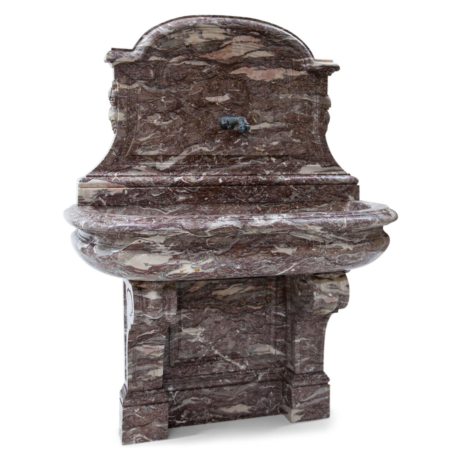 Lilac wall fountain out of hand carved Belgian marble. The basin is at a height of 95 cm and rests on volute supports; its interior dimensions are 15 x 112 x 38 cm. The wall is profiled. The rear wall shows a segment pediment with slightly concave
