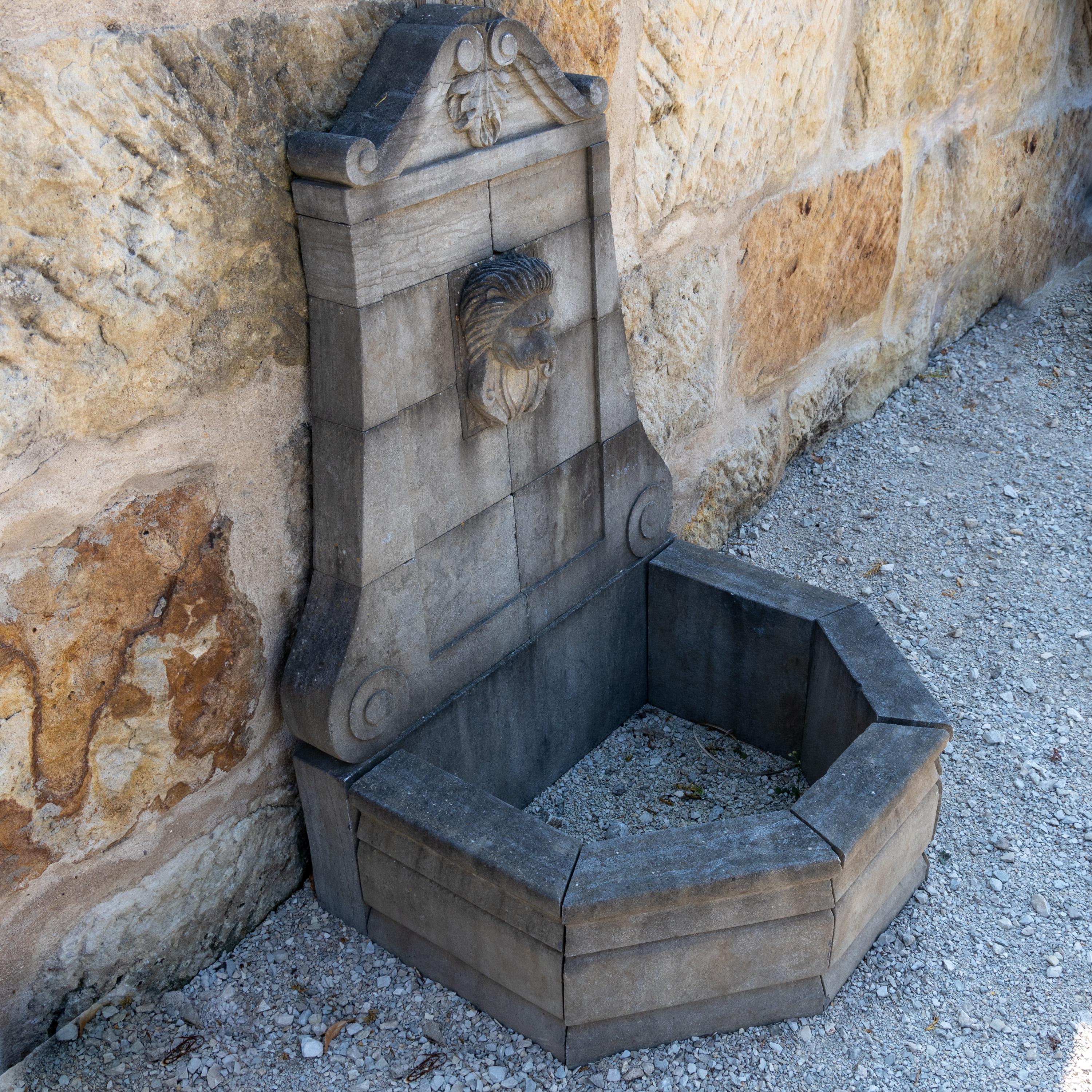 Wall fountain with hexagonal basin and curved back wall with central lion head as gargoyle. Hand carved bluestone.