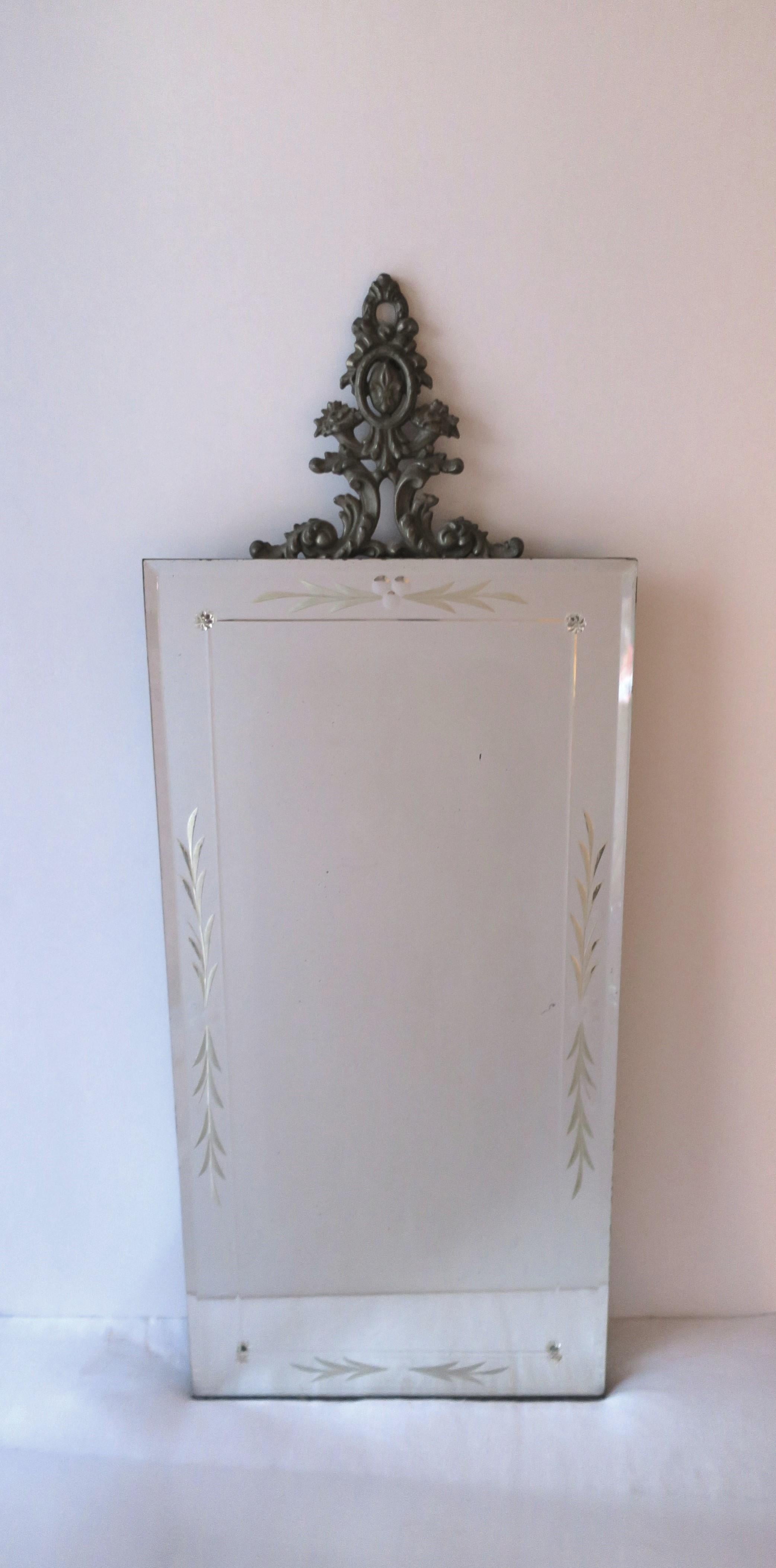 An etched wall mirror with metal ornamentation, in the Victorian style, circa early-20th century. A rectangular wall mirror with etched design, metal ornamentation at top (with flower, leaf, and fleur-de-lis design), and small glass rosettes at