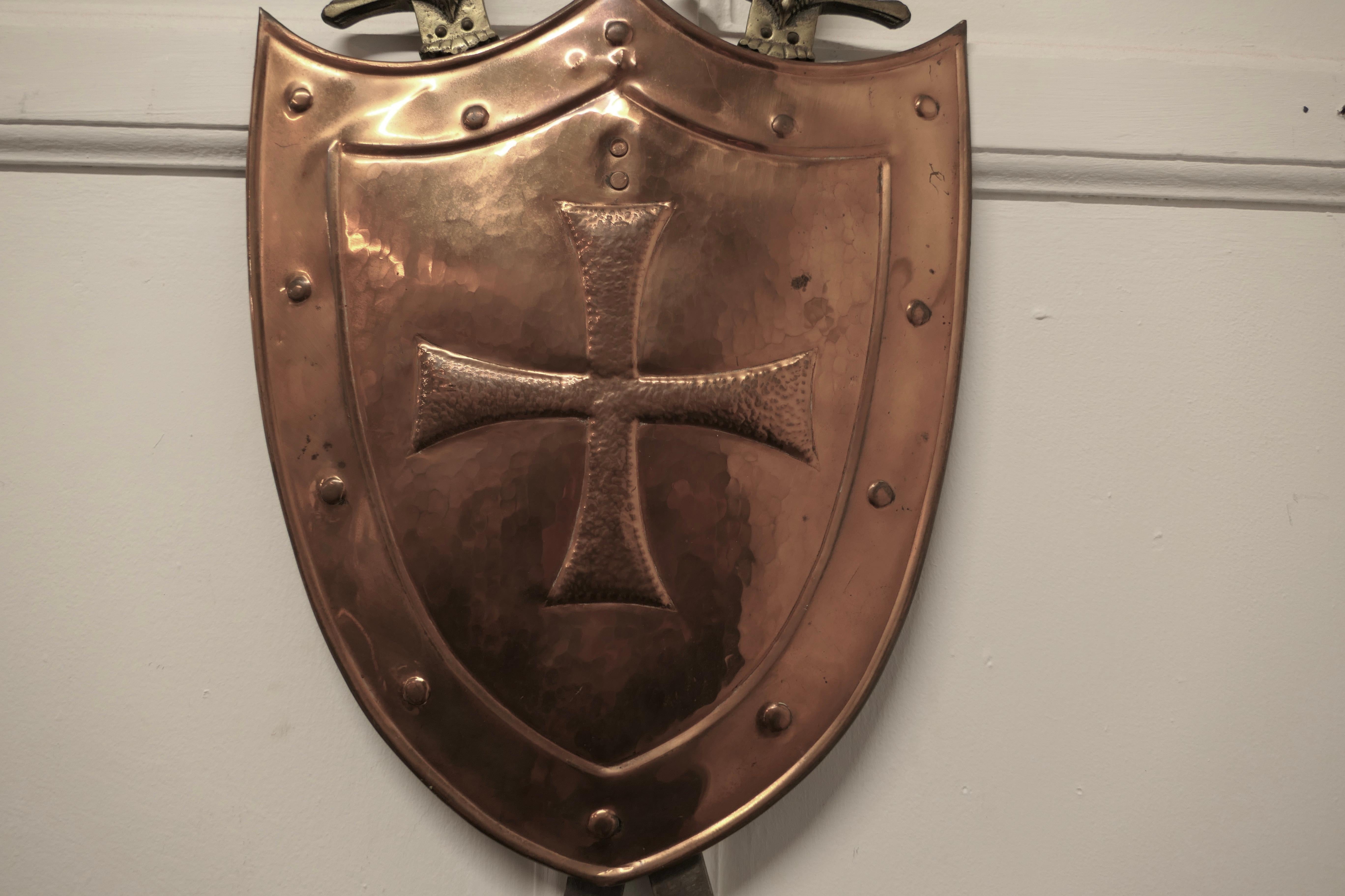 Wall hanging Arts and Crafts copper shield with cross swords 

A large decorative wall piece the shield is made in hand beaten copper and has a cross of the knights Templar 
The swords are held in the back but removable, a good looking piece of