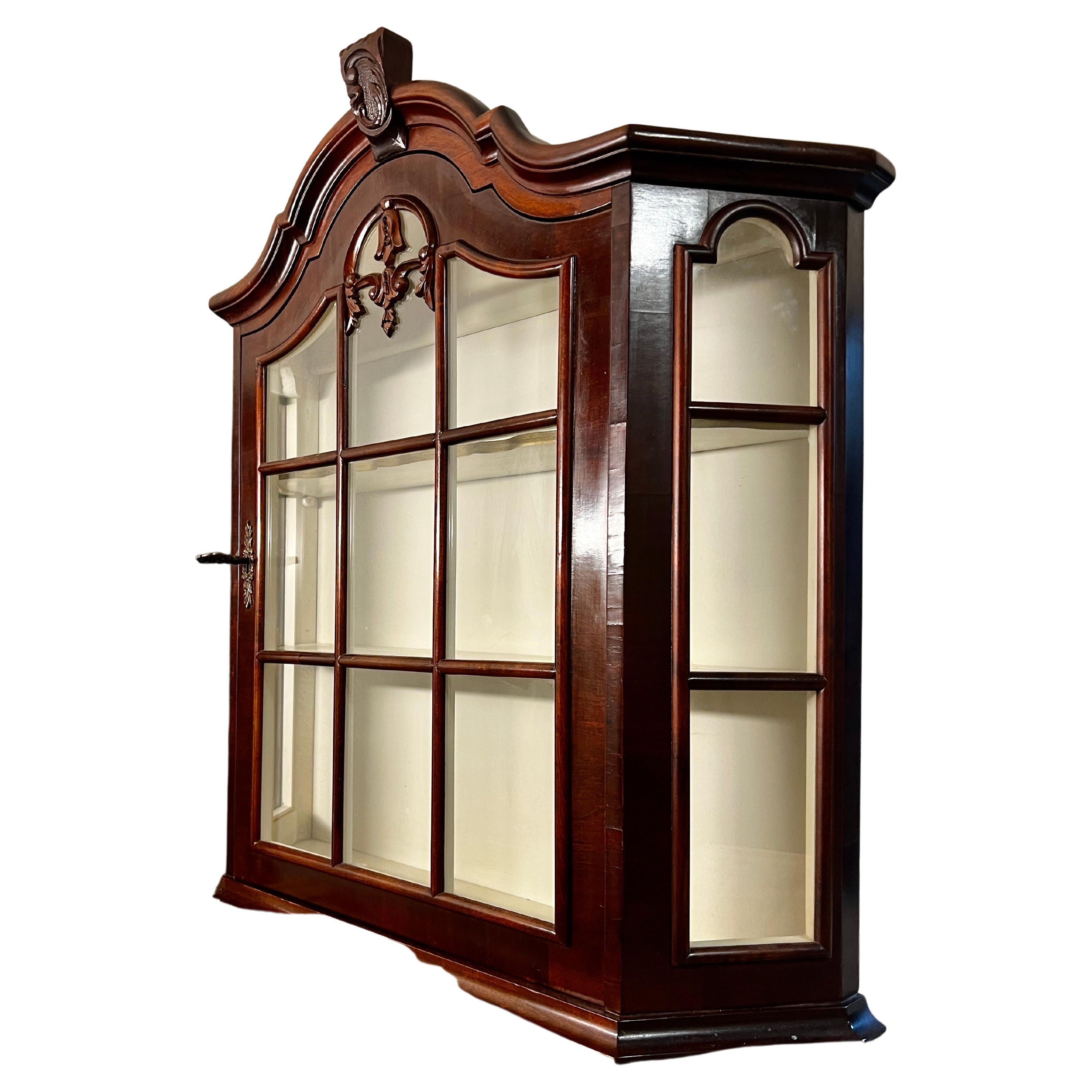 A delightful vintage glass front china or curio cabinet in Rococo Stylepossesses a beautifully carved pediment, allowing it to be displayed on a counter or wall-mounted with elegance. Made in 20th century and crafted in traditional mahogany,