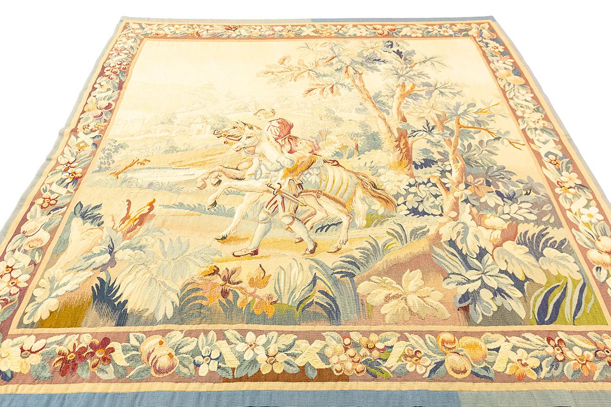 Dieser 176 x 174 cm große, wunderschön detaillierte beigefarbene Wandteppich ist eine exquisite Darstellung klassischer pastoraler Kunst, wahrscheinlich inspiriert von europäischen Landschaftsszenen. Der Wandteppich zeigt einen idyllischen Moment