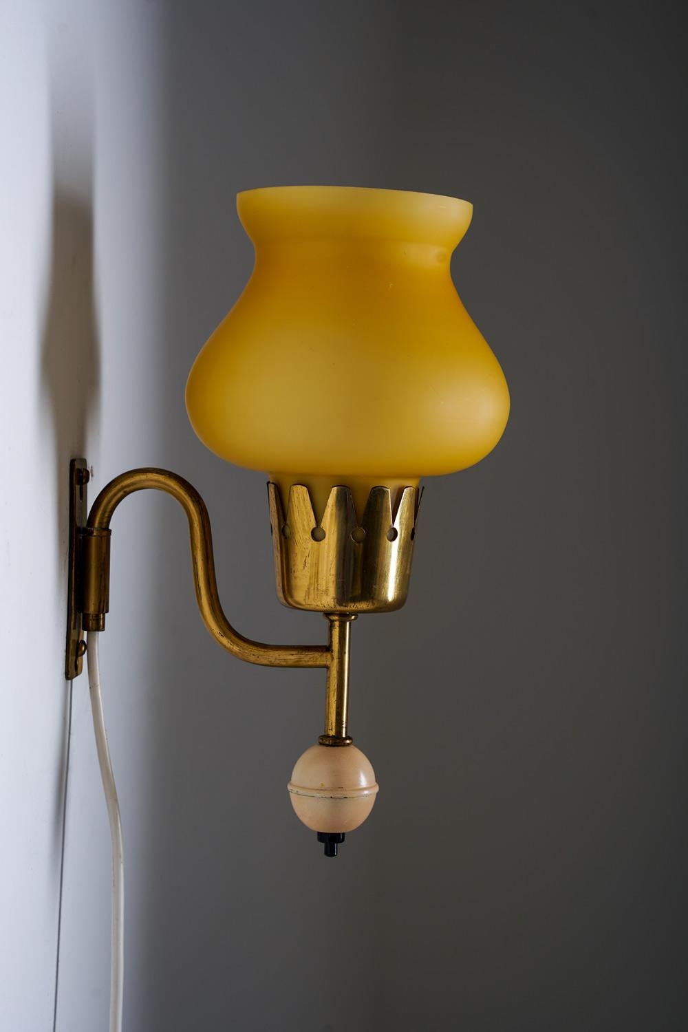 Encantadora lámpara de pared sueca diseñada por Erik Tidstrand para Nordiska Kompaniet (NK) en la década de 1950. La lámpara presenta un brazo de latón elegantemente curvado y una pantalla de cristal amarillo esculpido que emite una luz cálida y