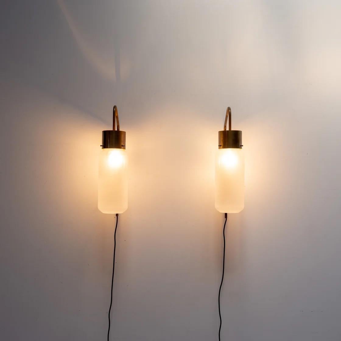 Elegante lámpara de pared diseñada por Luigi Caccia Dominioni para Azucena. Conocido como modelo Bidone, presenta una suave pantalla de cristal esmerilado suspendida de un brazo curvo de latón. Perfecto como acento cálido y minimalista en pasillos,