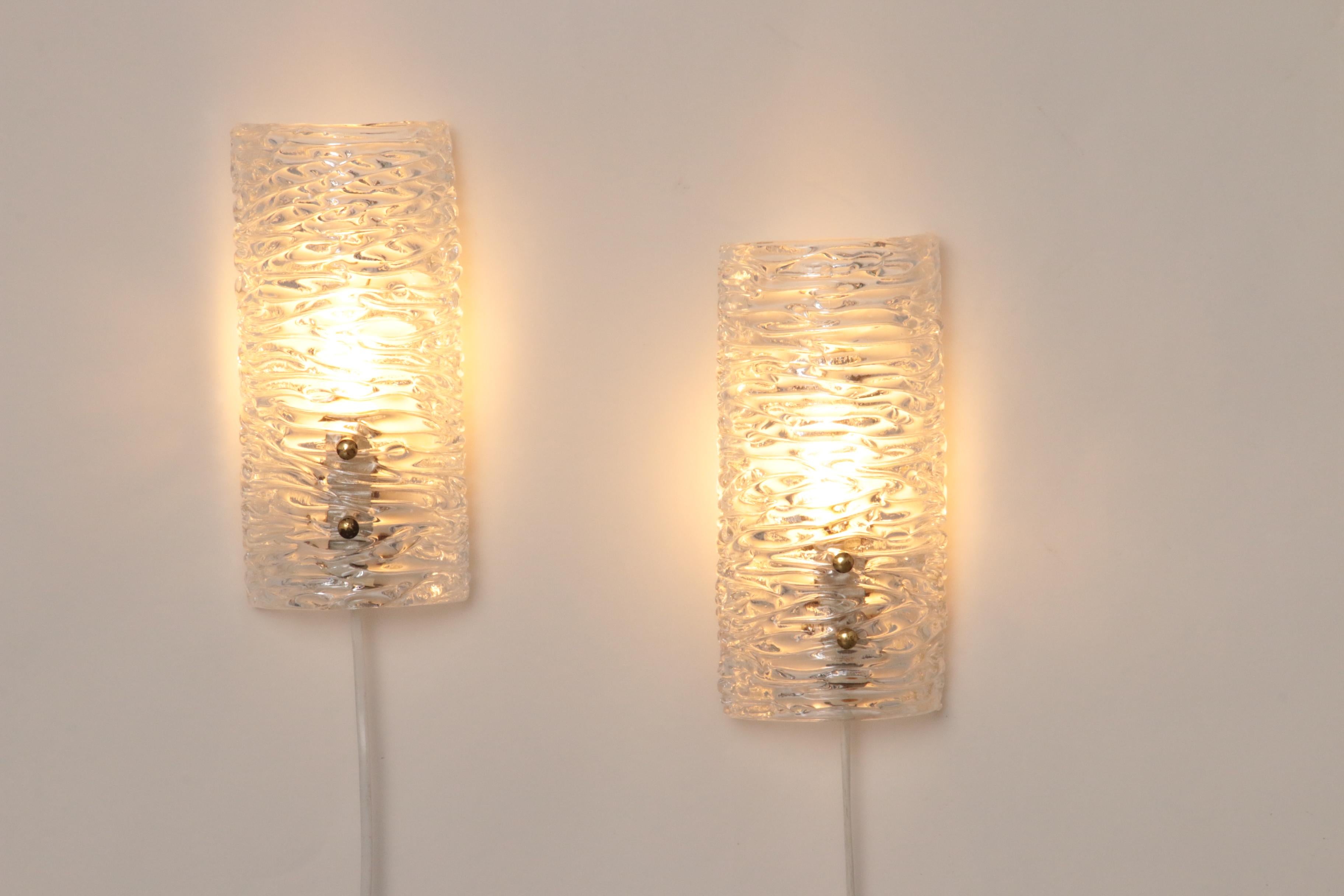 

Cette superbe lampe, conçue par Carl Fagerlund pour Orrefors,

se caractérise par un verre pressé épais avec une texture de glace en relief.

Le cadre en fer et les boutons dorés ajoutent une touche de sophistication, tandis que le verre en relief