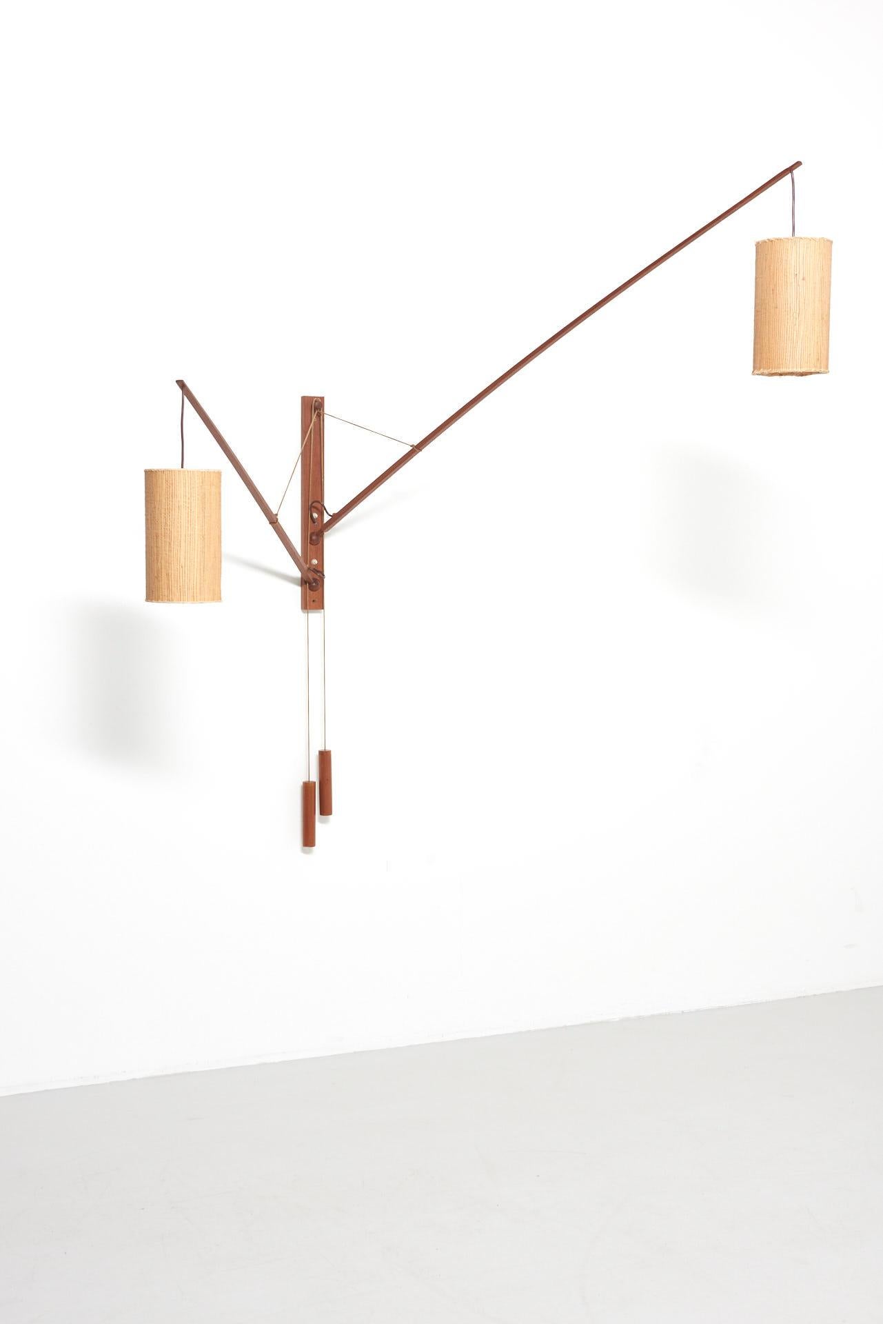 A teak wall lamp designed by Rupprecht Skrip in the 1950s. The two cantilevers are adjustable in all directions by balljoints and are held in position by counterweights. The two lamps with original shades in straw give a warm light and can be