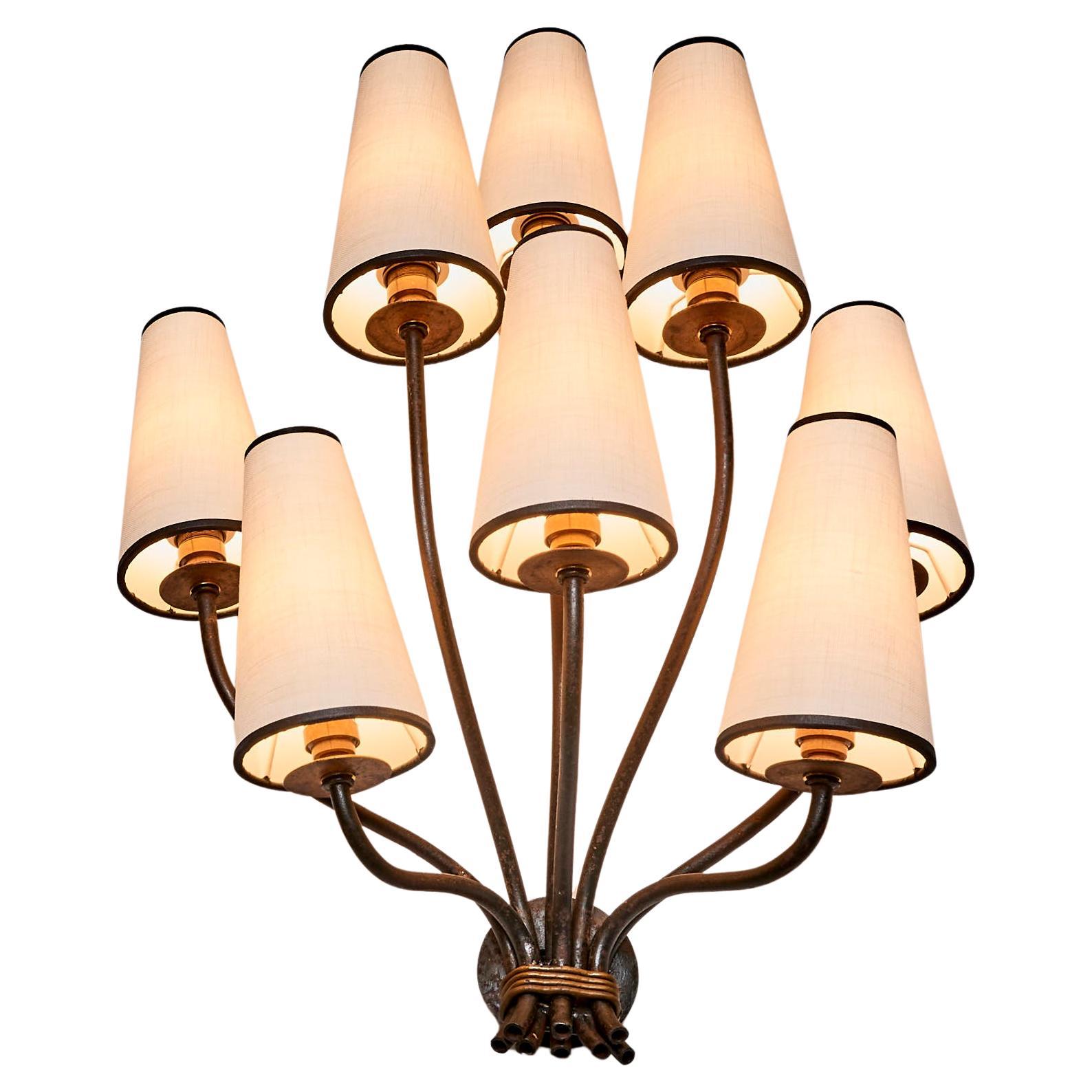 This is a wall lamp made in the manner of Jean Royere from the same period. The lamp features a bouquet of curved arms and a metal frame with a lovely patina.The fabric lampshades provide a soft, warm light, making this piece both functional and