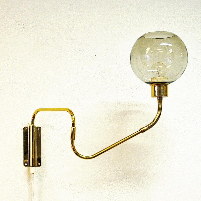 Midcentury wall lamp on an adjustable brass arm with a smoked glass dome by T. Røste & Co, Norway, 1960s. The lamp can be adjusted to the left, right, upwards, downwards and straight ahead. A great lamp for all rooms in good vintage