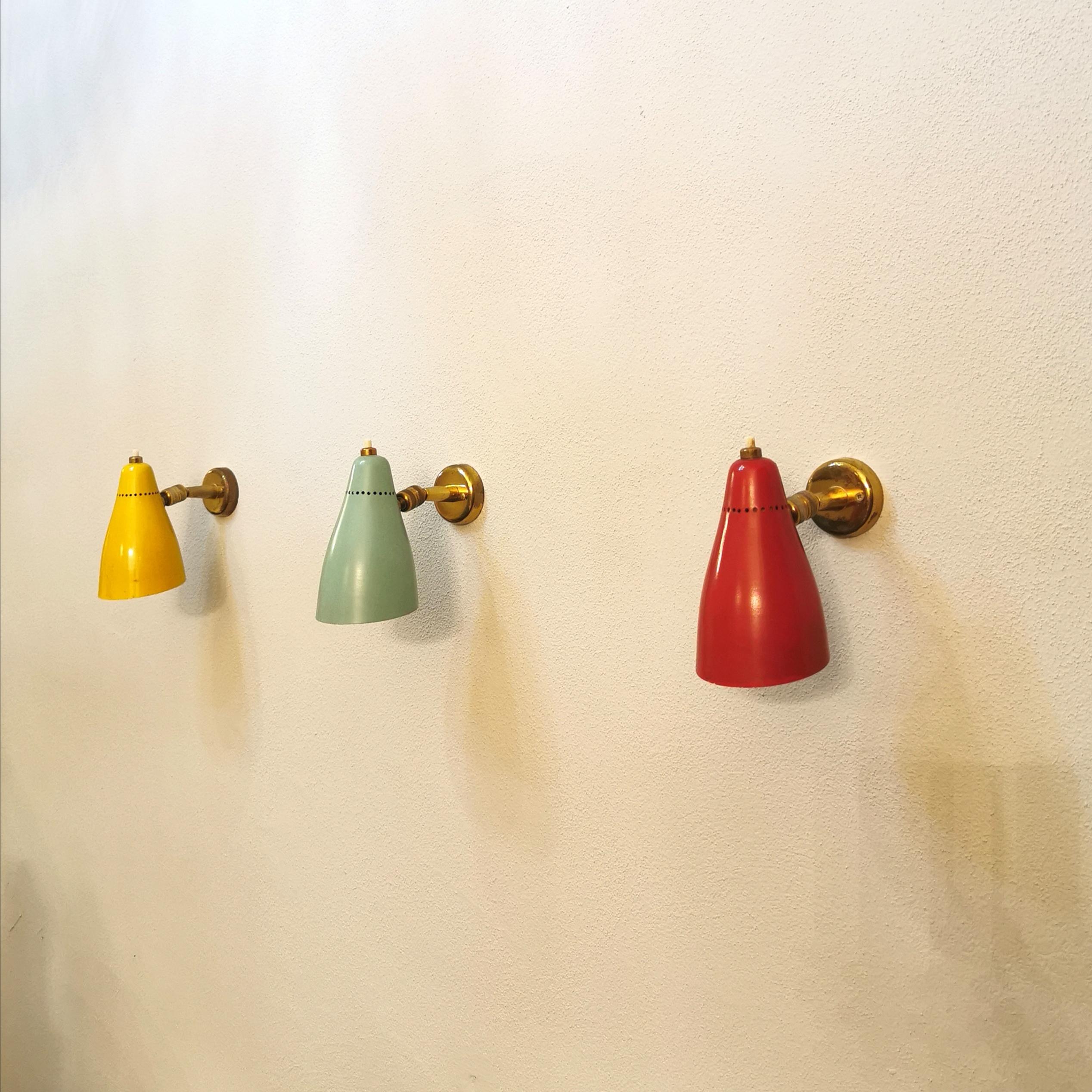 Set of 3 wall lamps designed by the Italian designer Giuseppe Ostuni in the 1950s. The lamps have a brass wall-mounted housing with yellow, green and red diffusers in conical enamelled aluminum, which can be directed thanks to the brass joints.