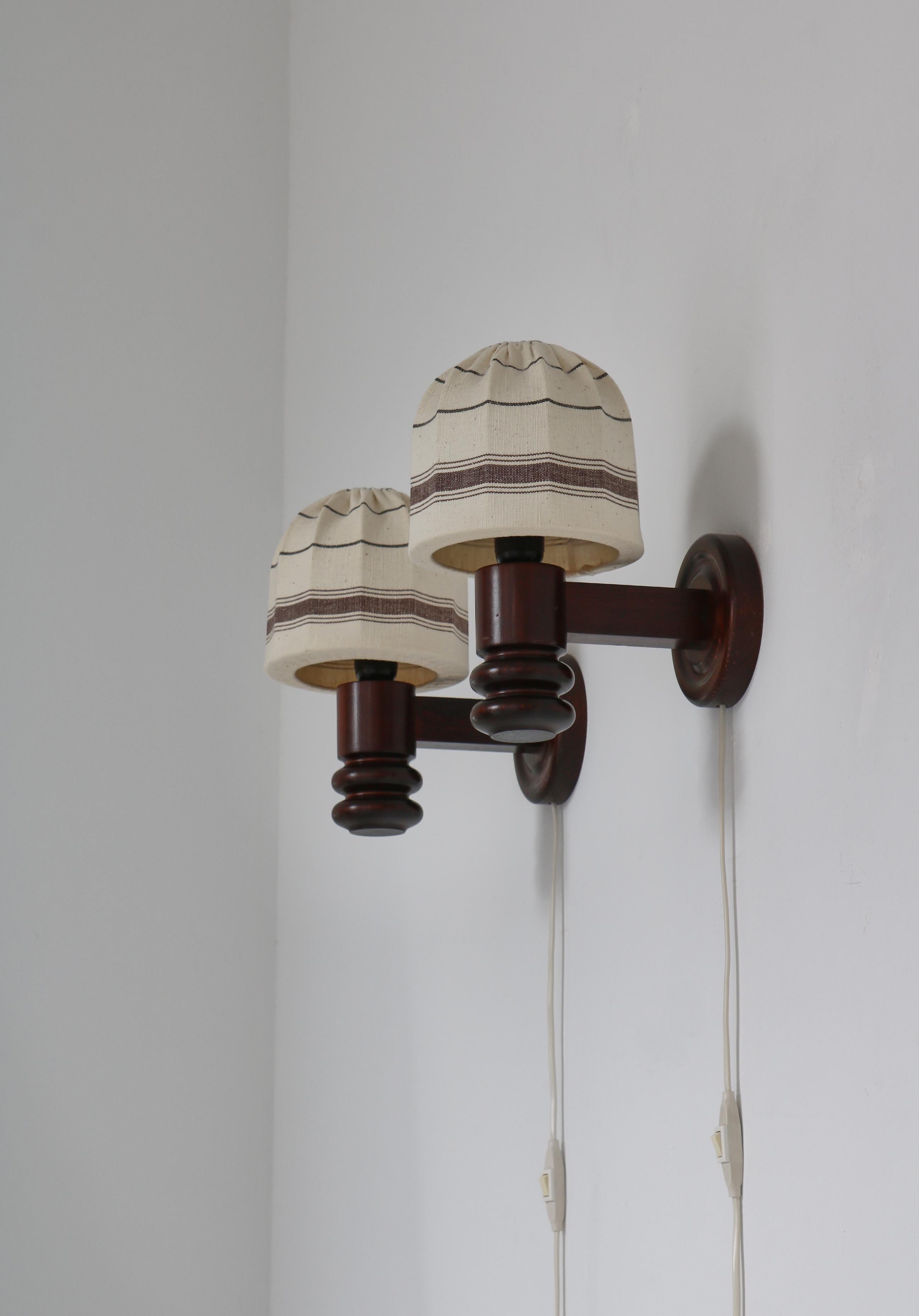 A pair of charming  vintage wall lights designed and produced by Solbackens Svarveri, Sweden in the 1970s. The wall mounts are made from dark stained Scandinavian pinewood and the original shades are handmade textile. The fixtures are in very good
