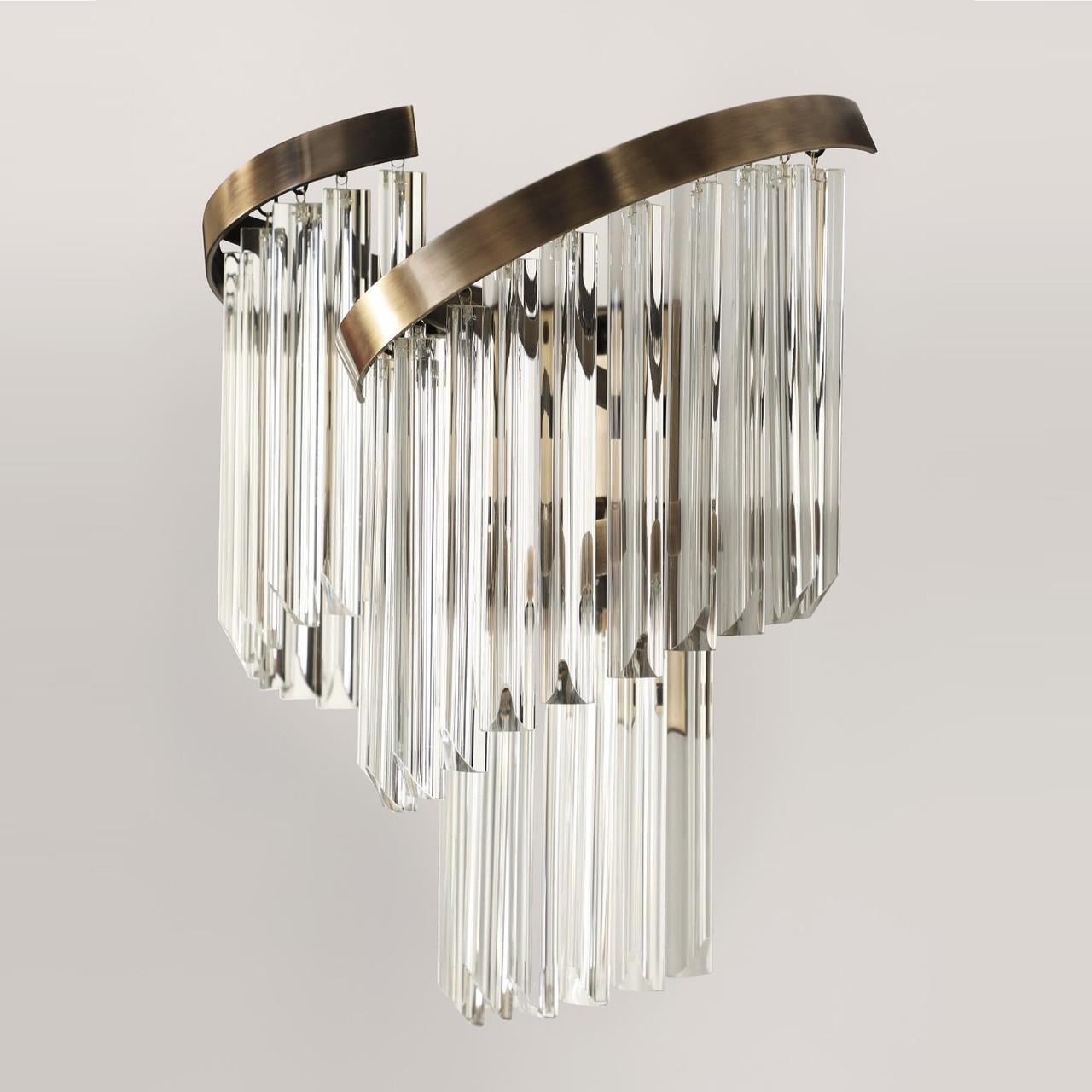 This wall lamp is a mesmerizing blend of artistry and functionality. Its inventive design features intertwined glass and gold-plated brass elements, exuding timeless elegance and sophistication. The dynamic interplay of materials and forms
