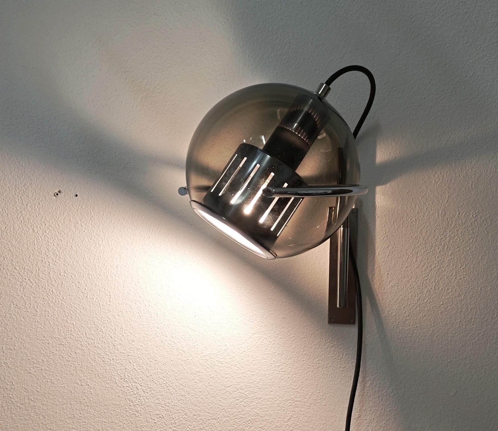 Wall lamp made in Italy in the 1960s and designed in the style of Luigi Caccia Dominioni.
The wall lamp features a brass and chrome-plated steel frame and a spherical smoked glass diffuser. The semicircle supporting the glass sphere rotates