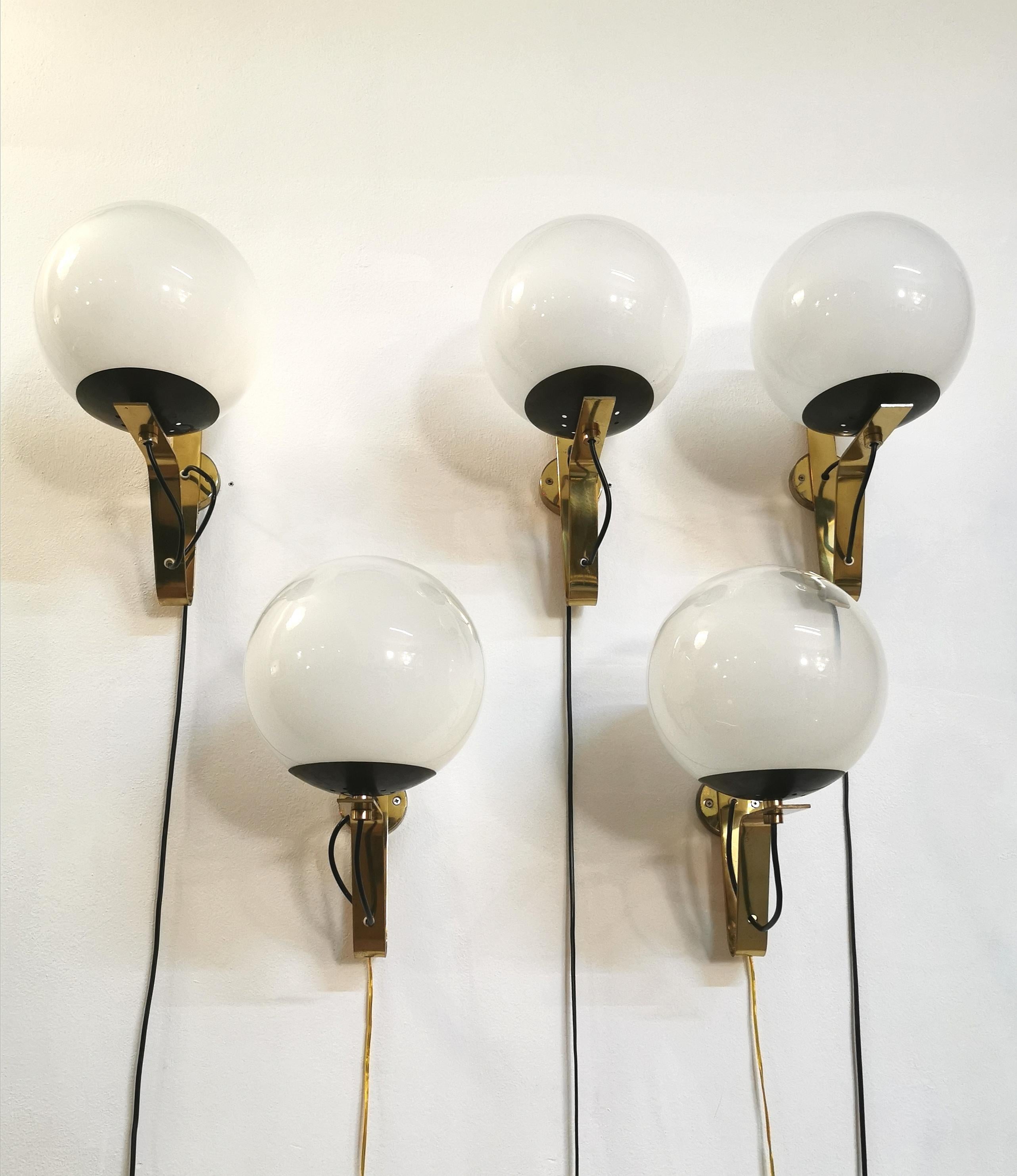Set of 5 wall lamps designed in the style of the renowned designer Gino Sarfatti between the 60s and 70s. Each single wall lamp has a structure with curved bands in brass with 1 E27 light that supports a particular white glass with a round shape