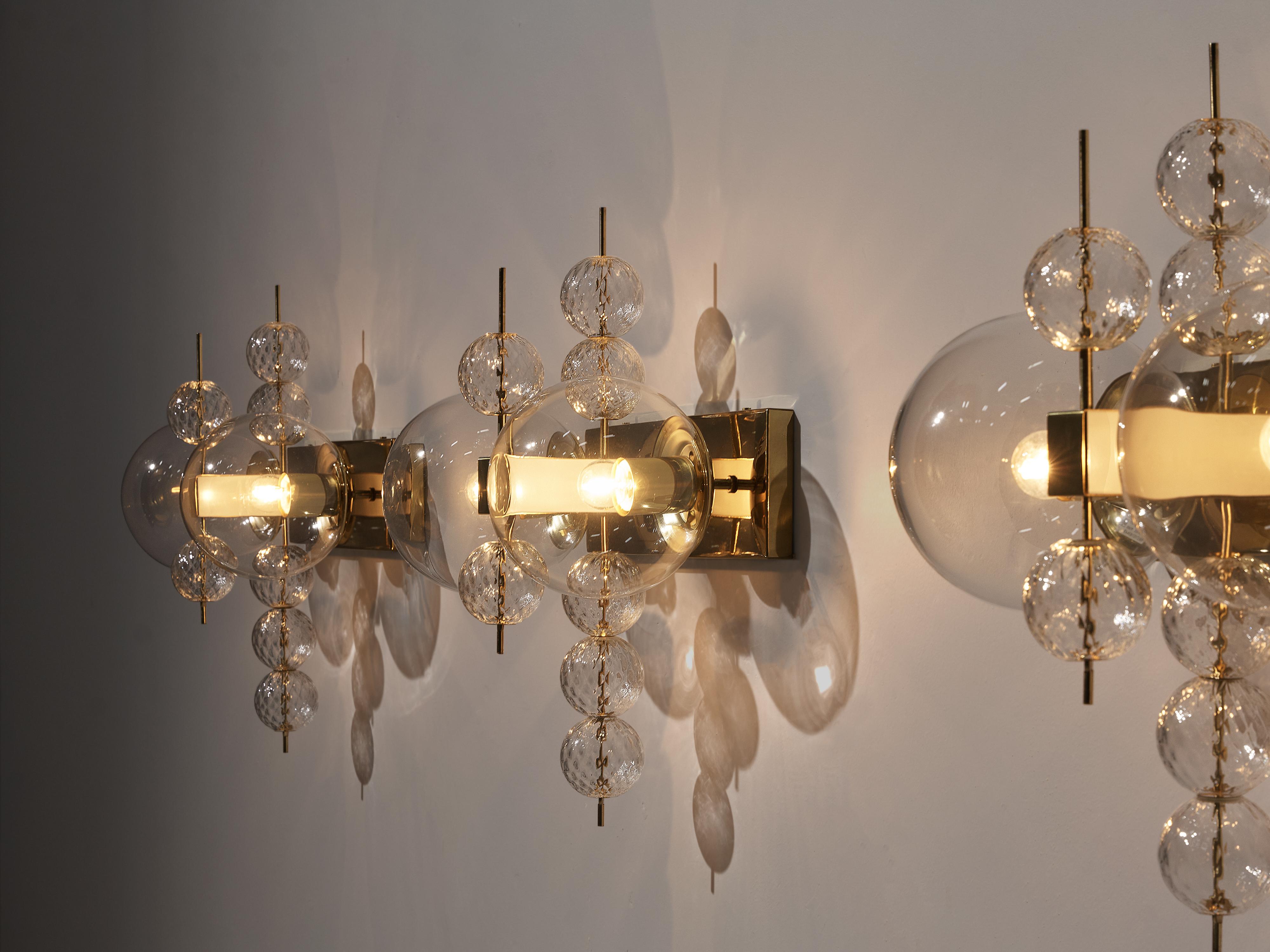 Wall lights, glass and brass, Europe, 1970s.

Ornate brass and glass wall light with two-light points and small decorative structured glass globes. The lamps are beautifully decorated thanks to the structured glass. The clear glass shades bring a