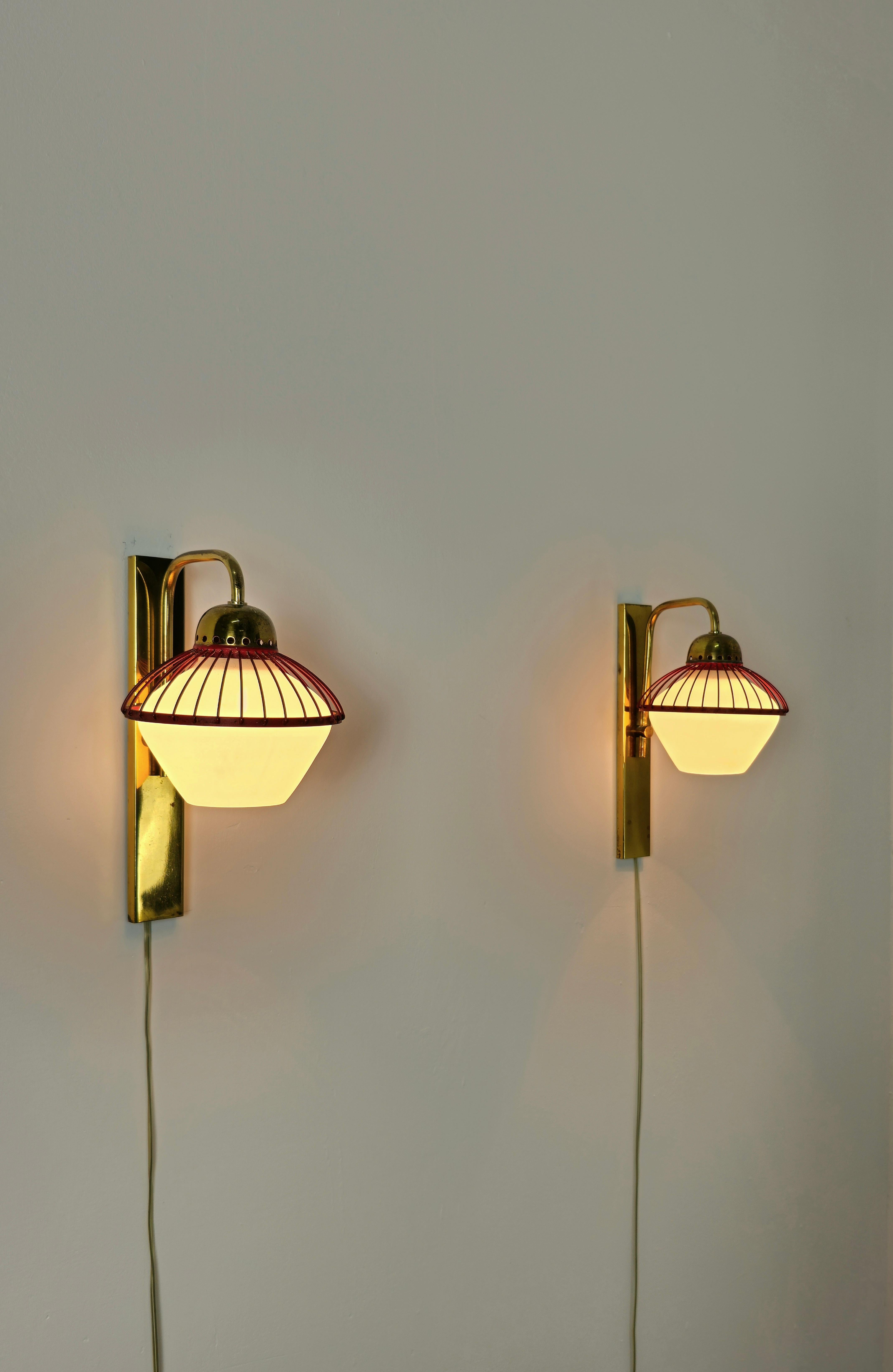 Satz von 2 Wandlampen, die Stilnovo zugeschrieben werden und in Italien in den 60er Jahren hergestellt wurden.
Jede einzelne Wandleuchte wurde mit einer Struktur und einem gebogenen Arm aus Messing, einem Zubehörteil aus rot emailliertem Metall und
