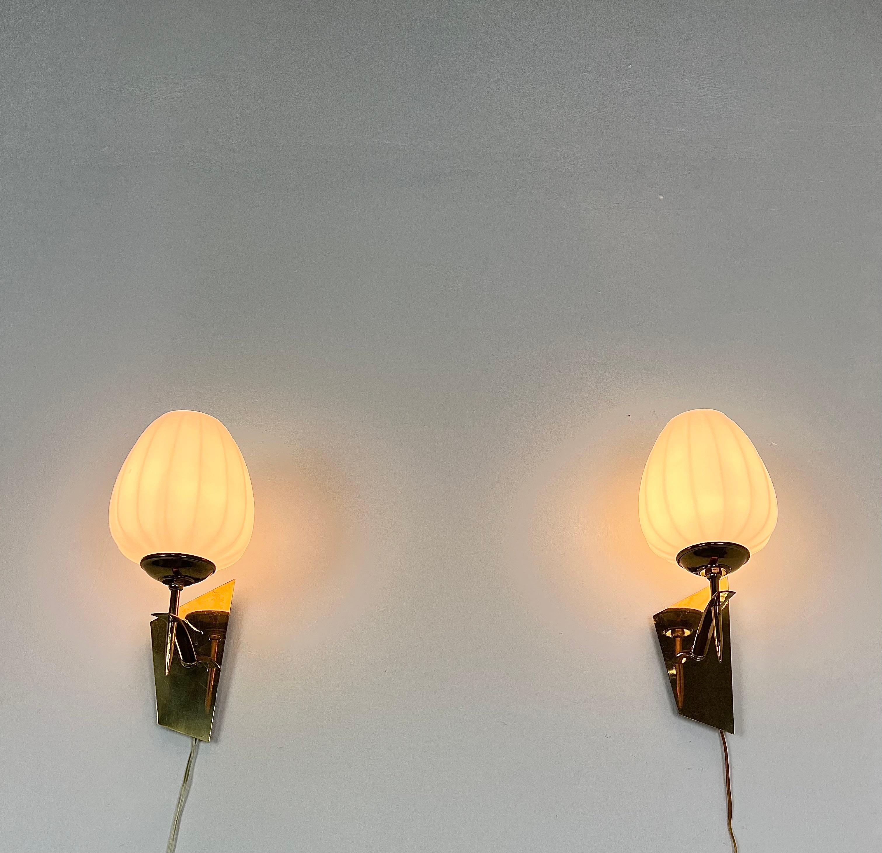 Set of 2 wall lamps made in Italy in the 1950s/60s and designed in the style of the renowned Stilnovo company. Each individual wall lamp was made with a brass structure with particular shapes that supports an opal glass diffuser.
