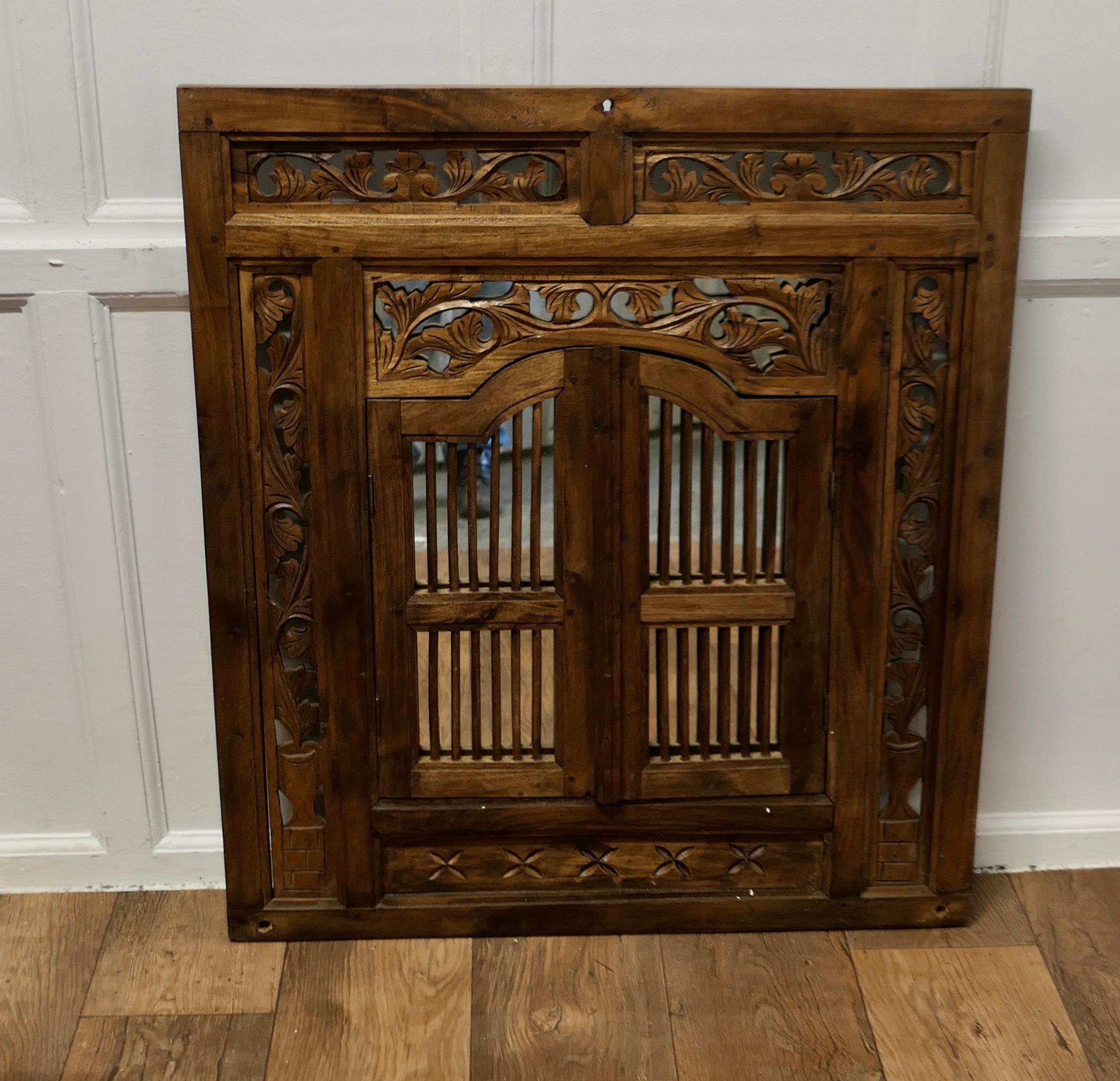 Wall Mirror Concealed by Heavy Carved Teak Door Shutters

This very attractive Carved Teak Double Door Frame conceals a mirror
The pair of doors have metal hinges and a wooden closer
A very sound and attractive piece 
The frame is 35” tall, 32” wide