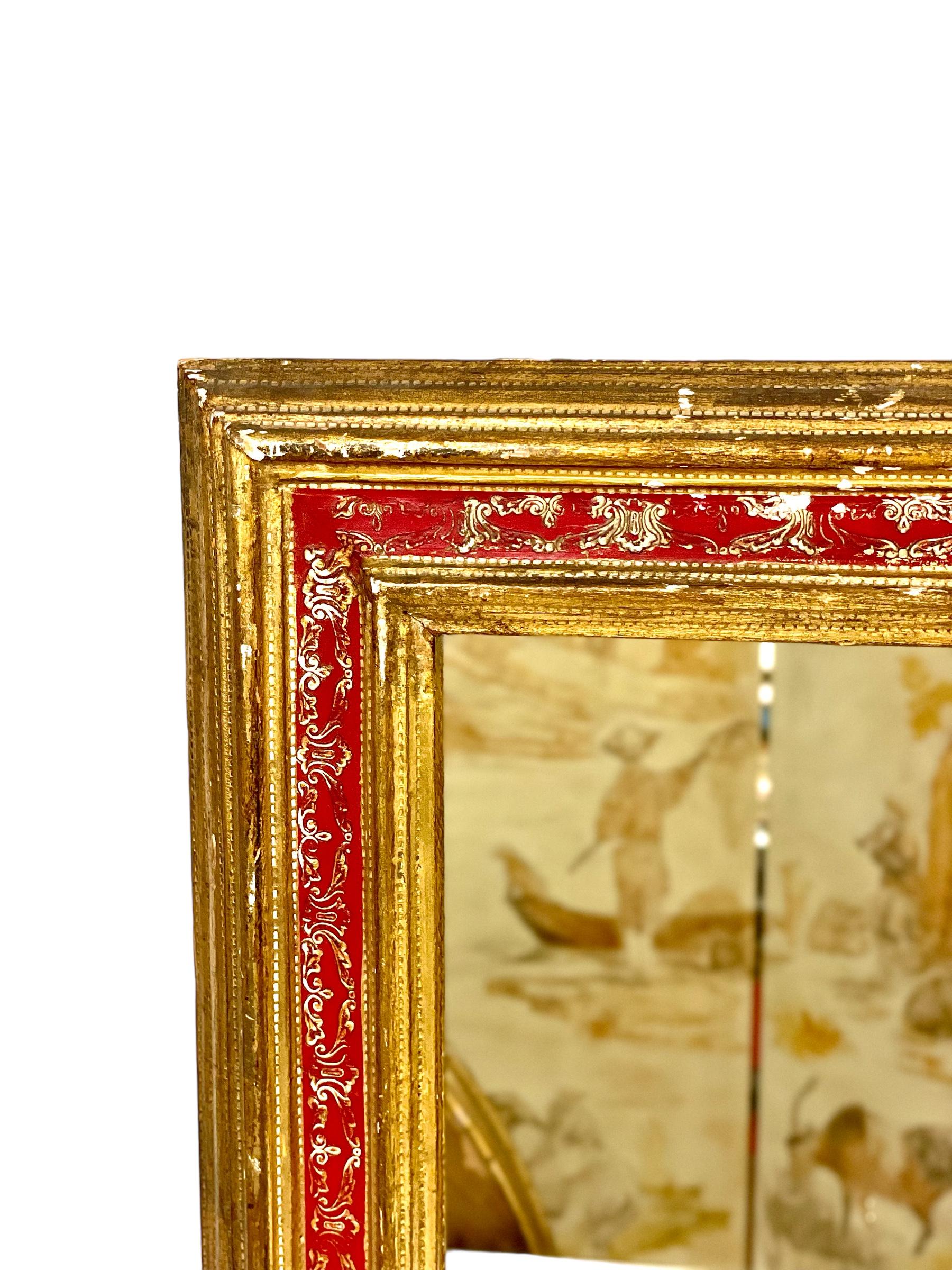 A very decorative wall mirror, in a gilt and red-lacquered wood frame. This small and very ornate mirror dates from the beginning of the 20th century, and its frame features multiple moulded undulations on either side of a striking central band of