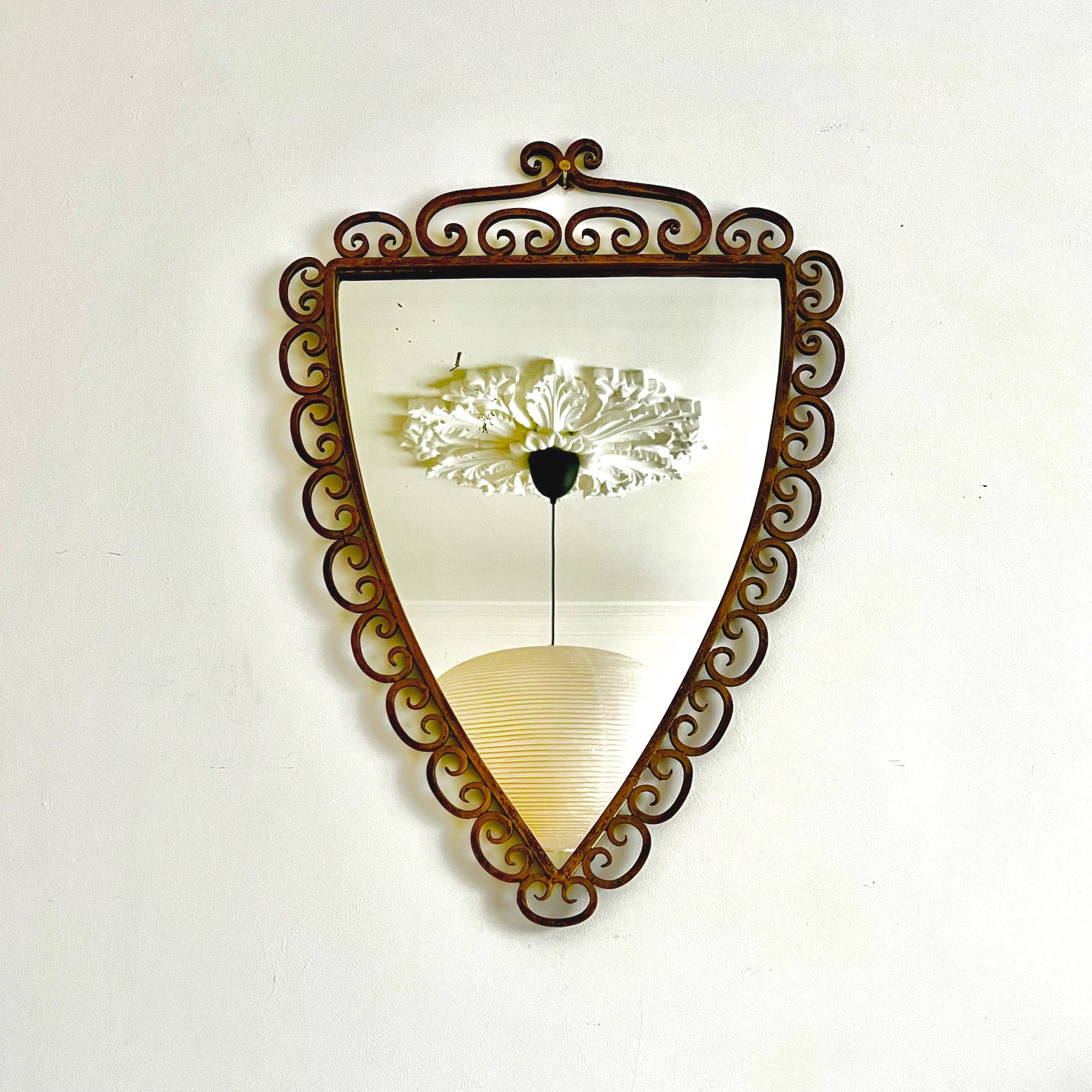 A wall mirror of soft triangular form, the wrought iron frame decorated with scrollwork with a painted finished in old . In the style of Pier Luigi Colli. Mid-20th Century. Found in Italy.

The mirror is nicely made with occasional irregularities in