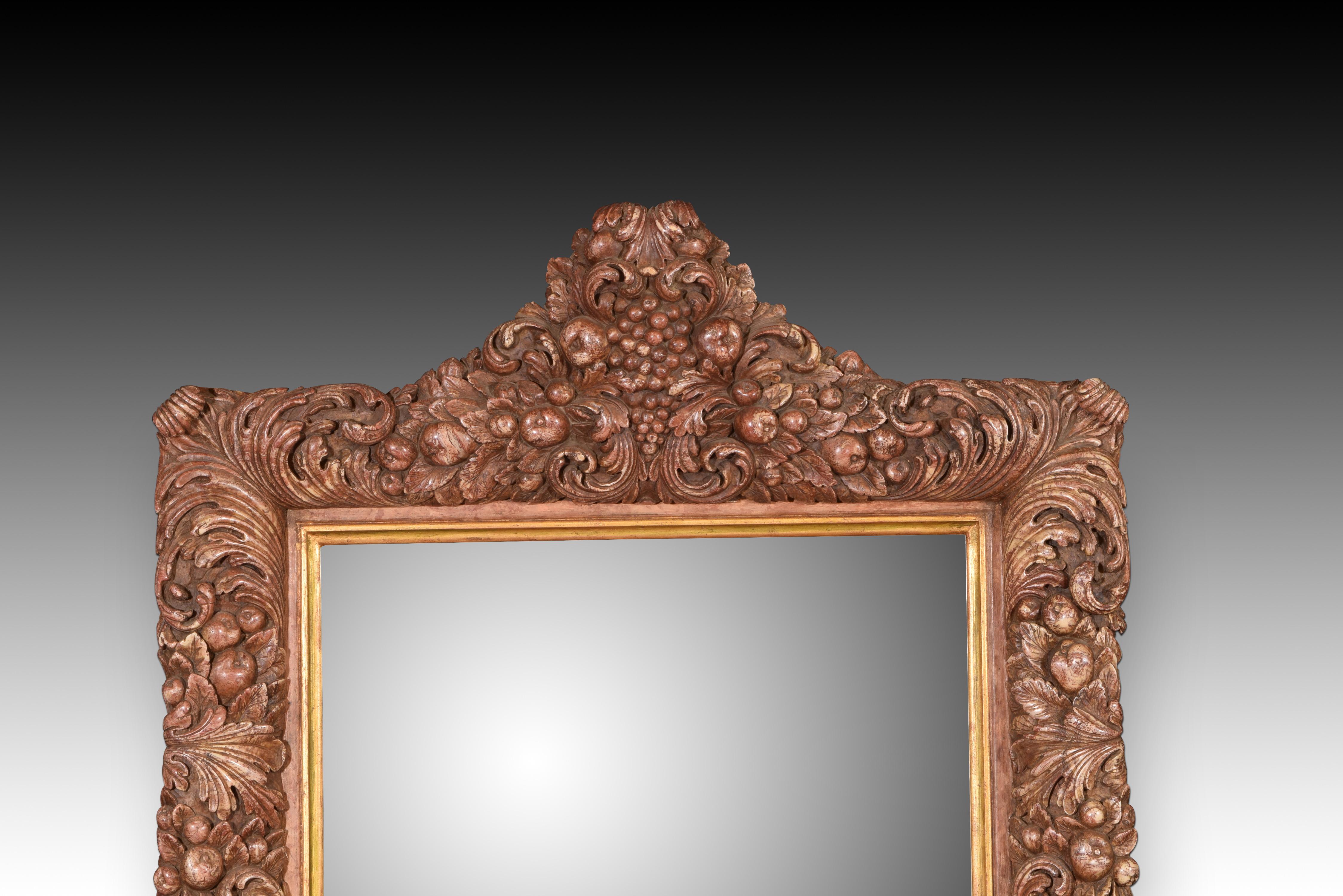 Wall mirror. Modeled alabaster. 20th century.  

Wall mirror with a frame made of modeled alabaster with polychrome, which has a decoration that resembles carvings based on plant and fruit elements, with a crest on the top. The work is inspired by