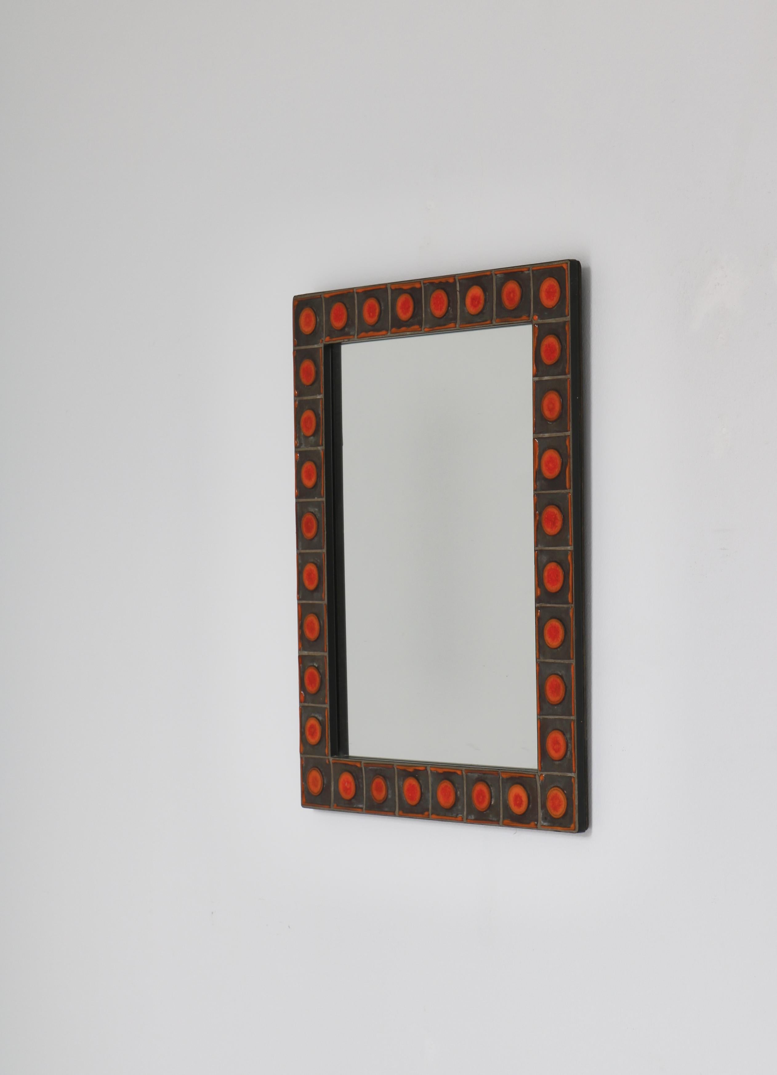 Beautiful wall mirror with orange decorated ceramics tiles  by Dietlinde Hein in the 1960s. The mirror was manufactured by Knabstrup ceramics workshop in Denmark.