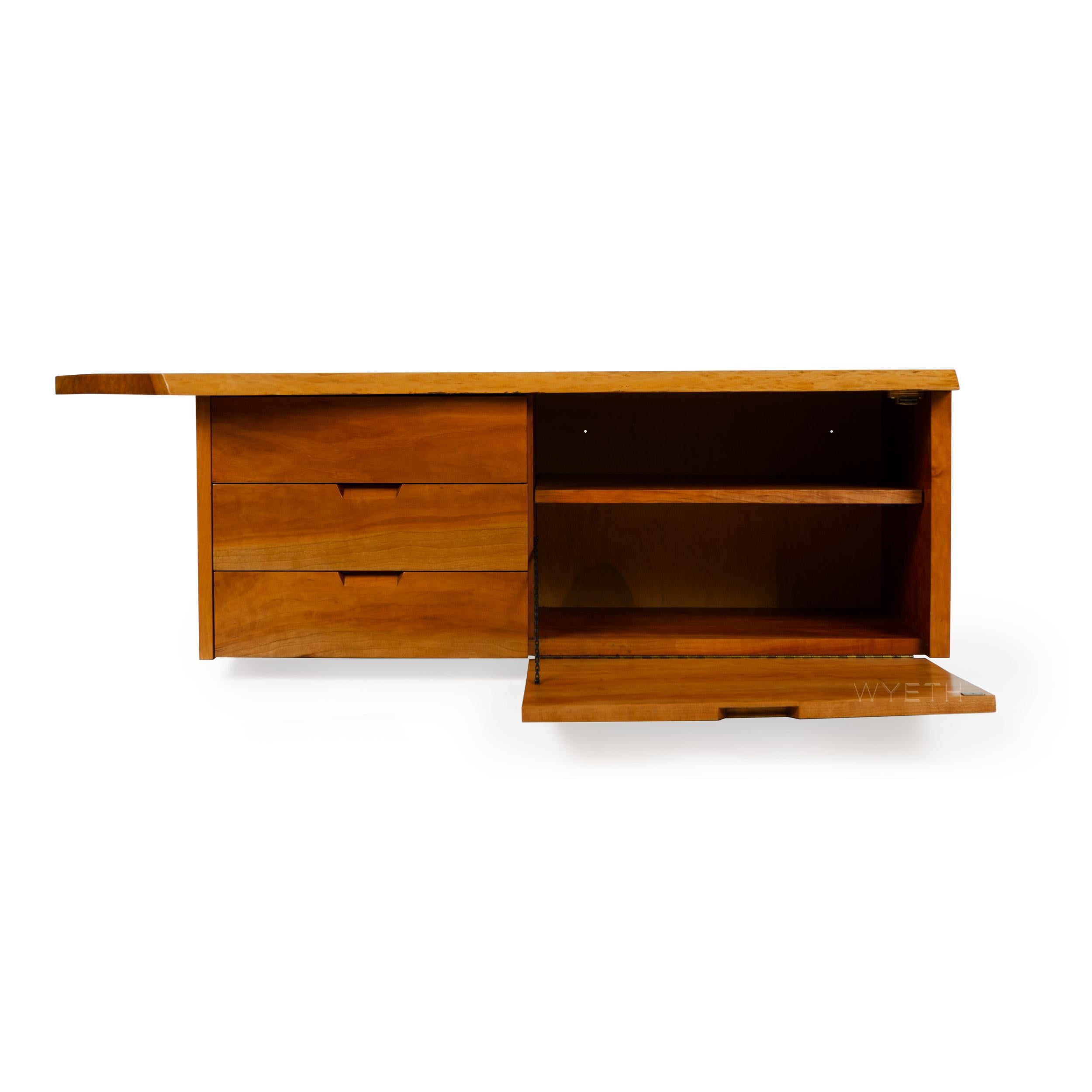 A walnut wall mount cabinet with one drop down door with an adjustable shelf and three (3) drawers, all with integrated handles.