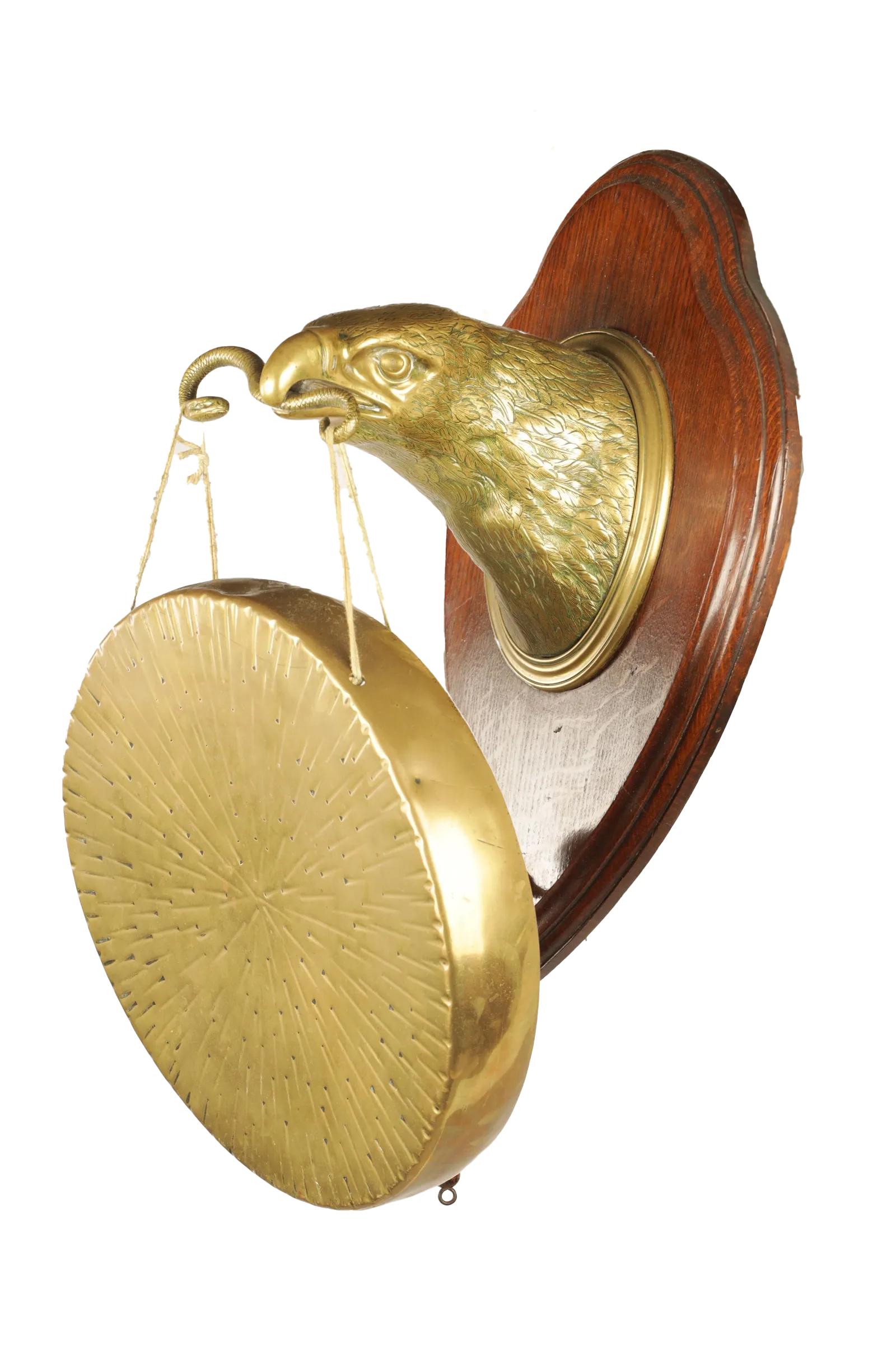 Gong de table de William Tonks & Sons (estampillé au dos), d'époque Arts and Crafts anglaise. Tête d'aigle en laiton ou en bronze bien fondu, montée sur une plaque de chêne en forme de bouclier et tenant un serpent dans son bec. Le serpent forme les