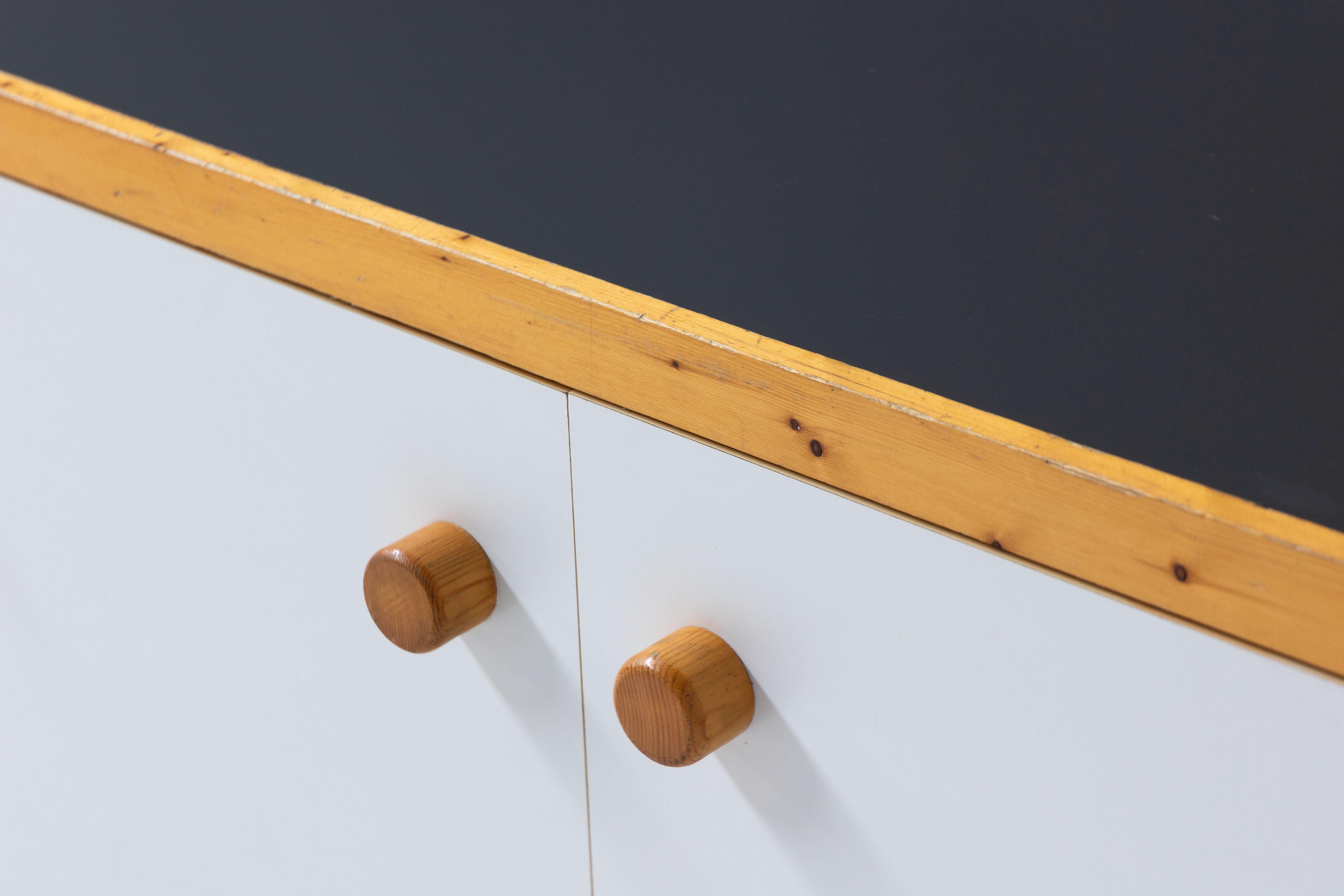 Armoire murale conçue par Charlotte Perriand pour la station de ski des Arcs en France. Cette superbe armoire à 3 portes allie la beauté du pin massif, du stratifié et des panneaux laqués plaqués pour créer une remarquable pièce d'art fonctionnelle.