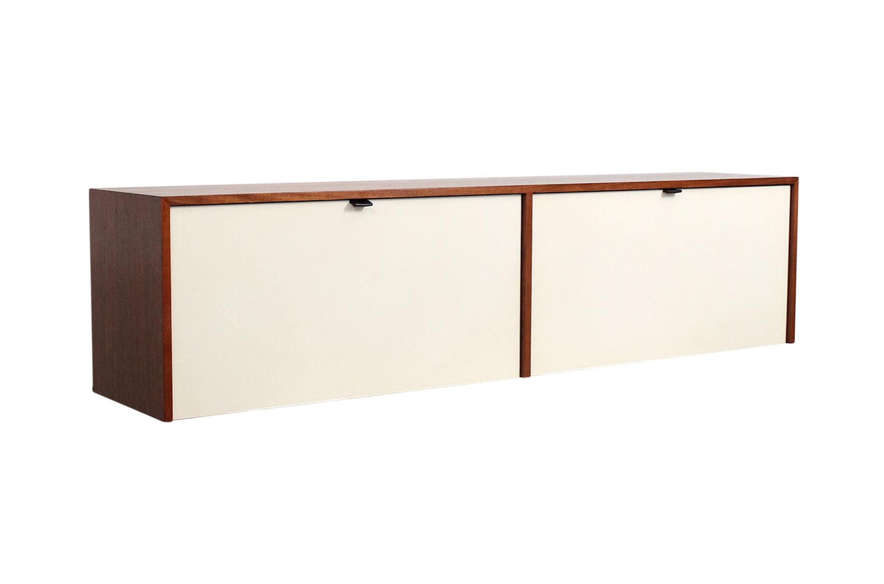 Wall-mounted cabinet by Florence Knoll for Knoll Associates. Walnut case with original white lacquered doors and interior. Interior has shelves of both oak and glass. This is cabinet model 