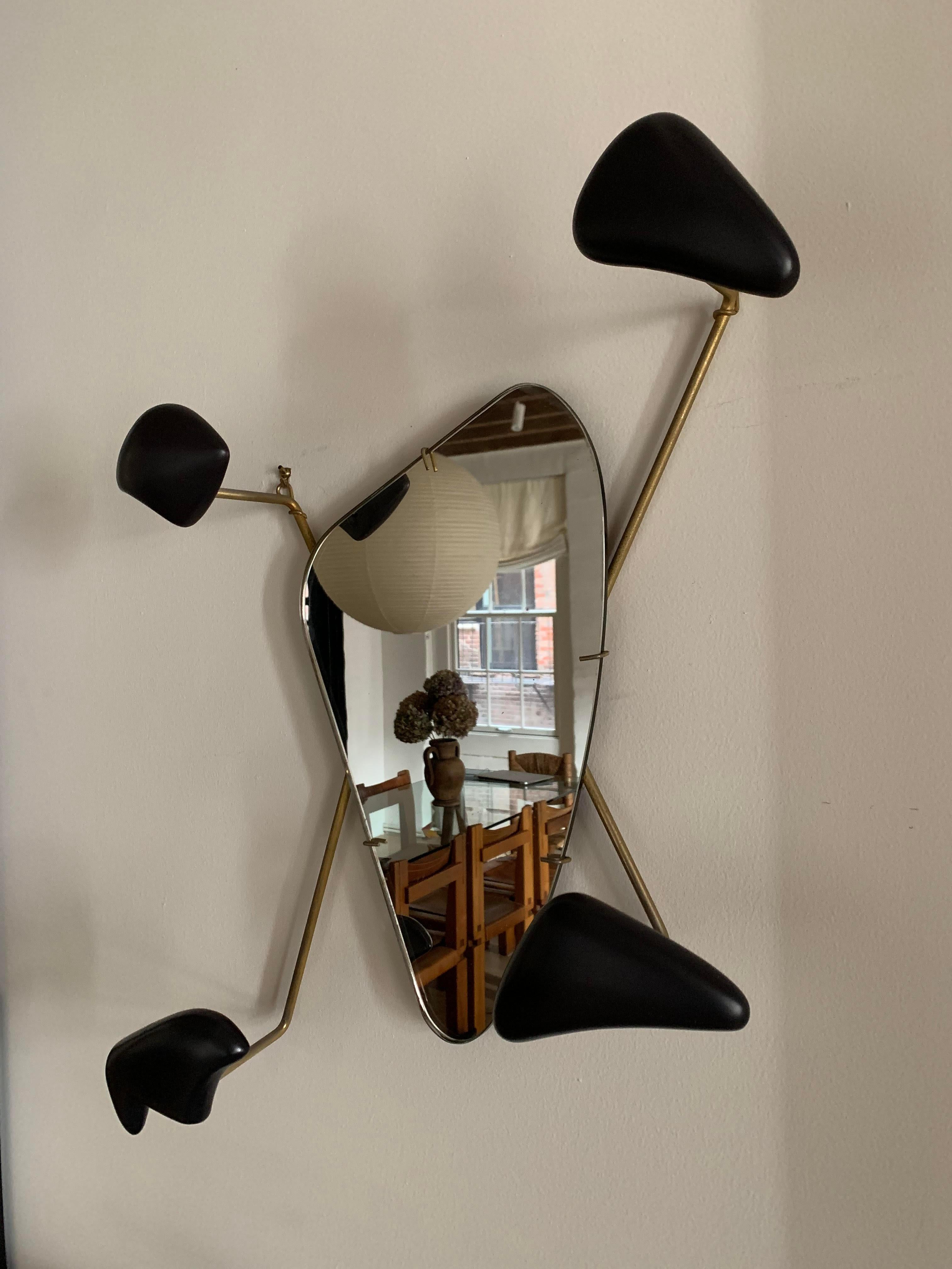 Vintage, sculptural wall-mounted coat rack with mirror by Georges Jouve and Marcel Asselbur. 

4 black, ceramic hooks with gilded metal arms attached to mirror. Each arm supports the weight of a hat or coat. 
 