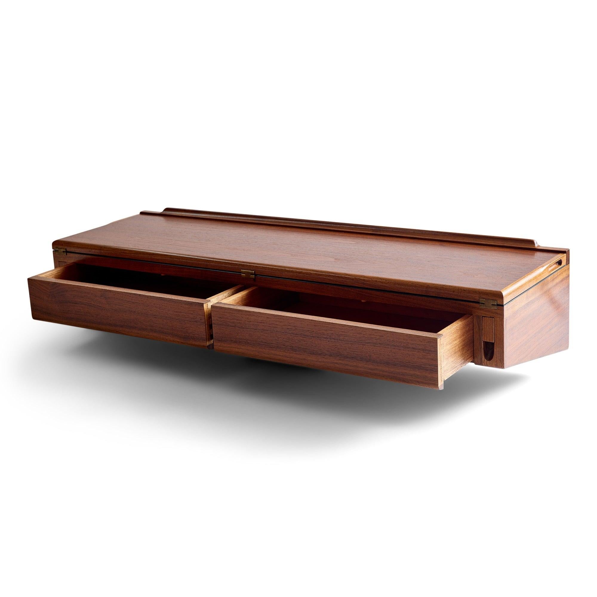 Cette console murale élégante et raffinée en teck riche est dotée de deux tiroirs encastrés et d'un plateau articulé (révélant une surface en stratifié noir avec de jolies charnières en laiton apparentes), ce qui permet à la pièce de servir