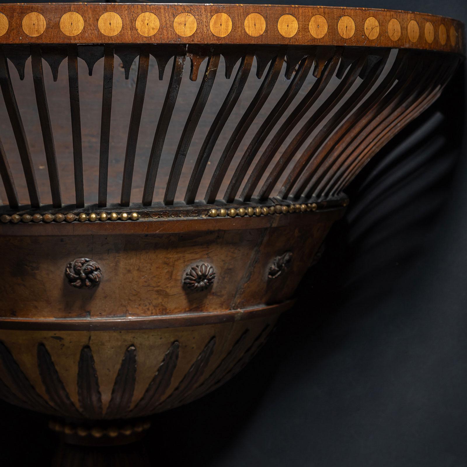 A vase-shaped, semi-circular flower basket from the 19th century. The wall is adorned with intricate leaf motifs and rosettes, defined by vertical struts. A narrow beaded brass band adds detail, though there are some minor losses.
The veneered