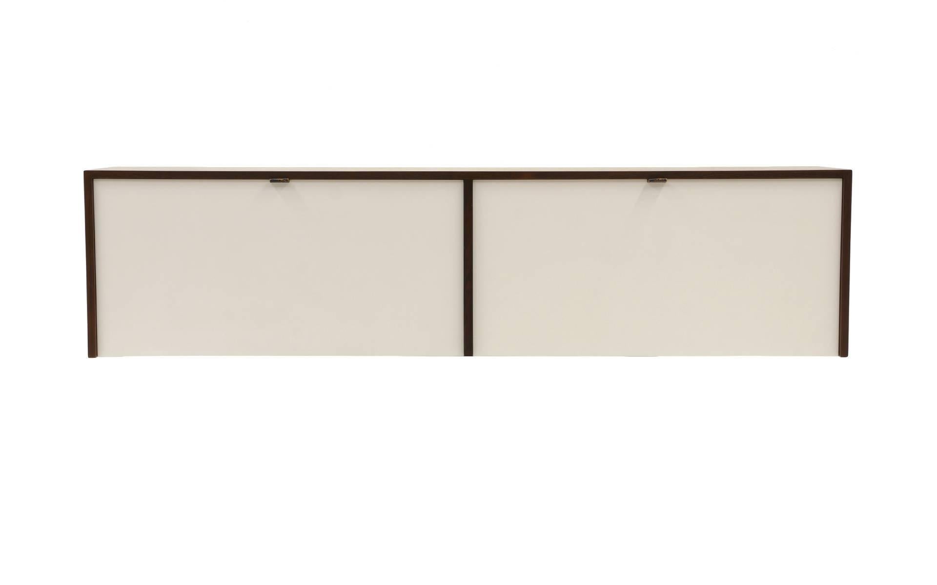 Zwei Wandschränke oder Kredenzen aus Palisanderholz, entworfen von Florence Knoll für Knoll. Frühe Produktion aus brasilianischem Palisanderholz mit weiß lackierten Türen, Innenräumen und Einlegeböden. Ein Schrank mit herunterklappbaren Türen, die