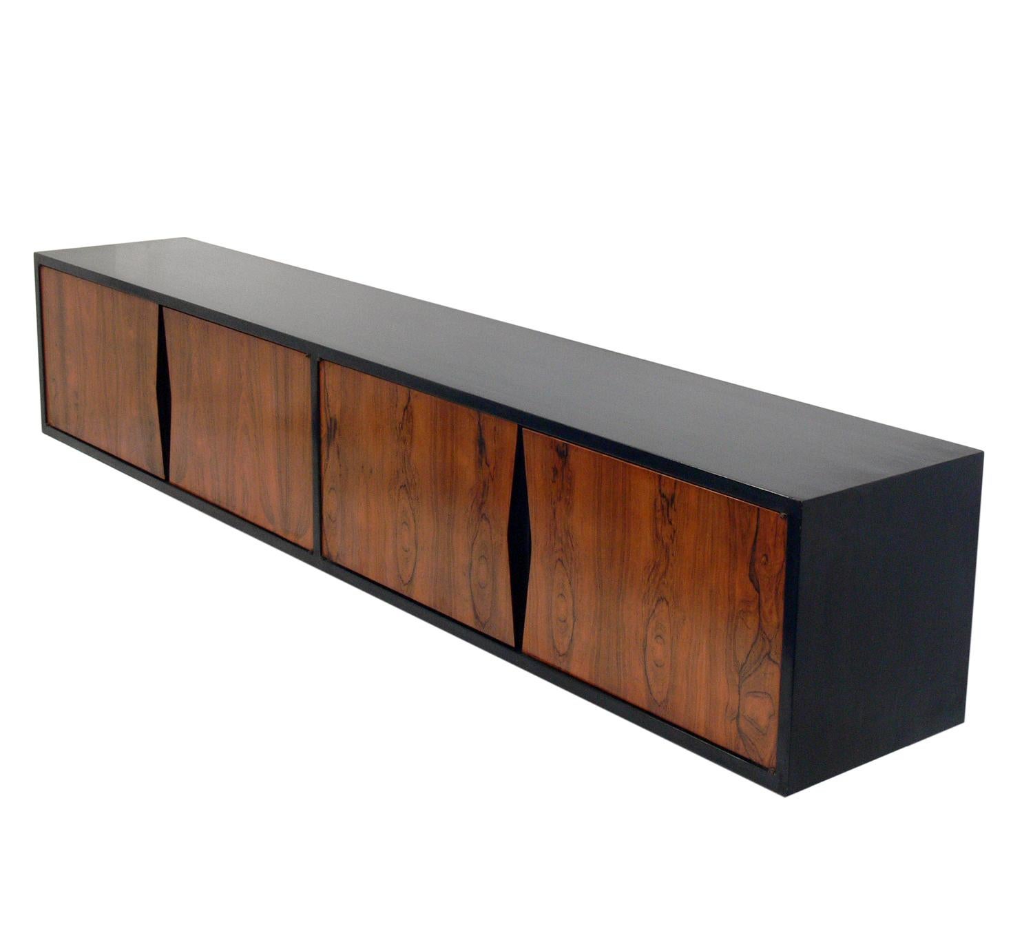 Wall-mounted rosewood console, American, circa 1960s. This piece is a versatile size and can be used as a console table, credenza, media cabinet for your TV, or as a vanity or desk. It is constructed of black lacquered wood and rosewood with a low