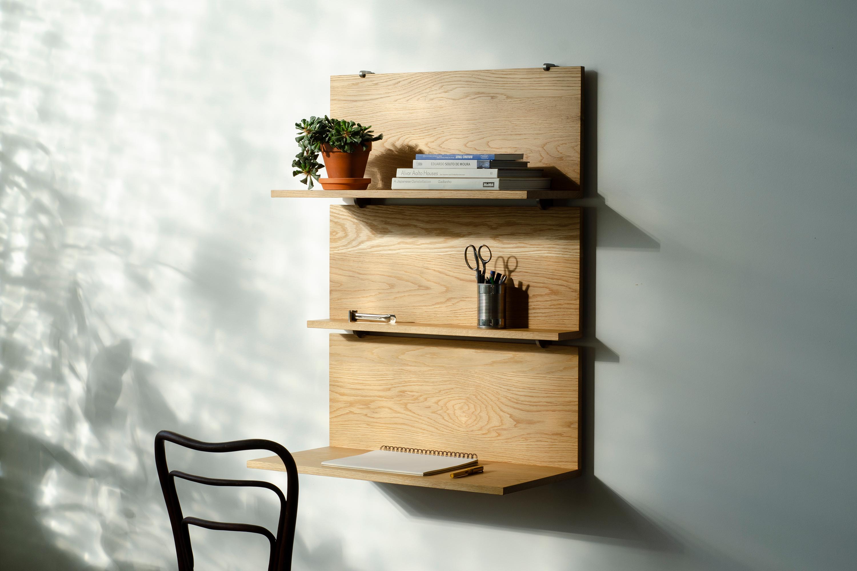 Wall anchored stainless steel rails support three wood shelves of varying depths. Each shelf serves a different function: shallow for small objects and pictures, medium for books and larger objects, and deep which serves as a desktop. Each clips