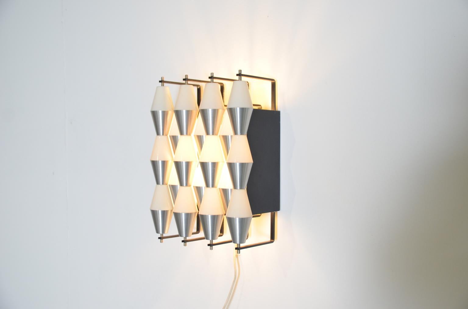 Model c-1656 by RAAK Amsterdam is symmetrically designed and consists of '18 little boxes, half opal and half matted silver lined up together to illuminated wall decorations' according to the original text in the RAAK catalogue. The lamp has two