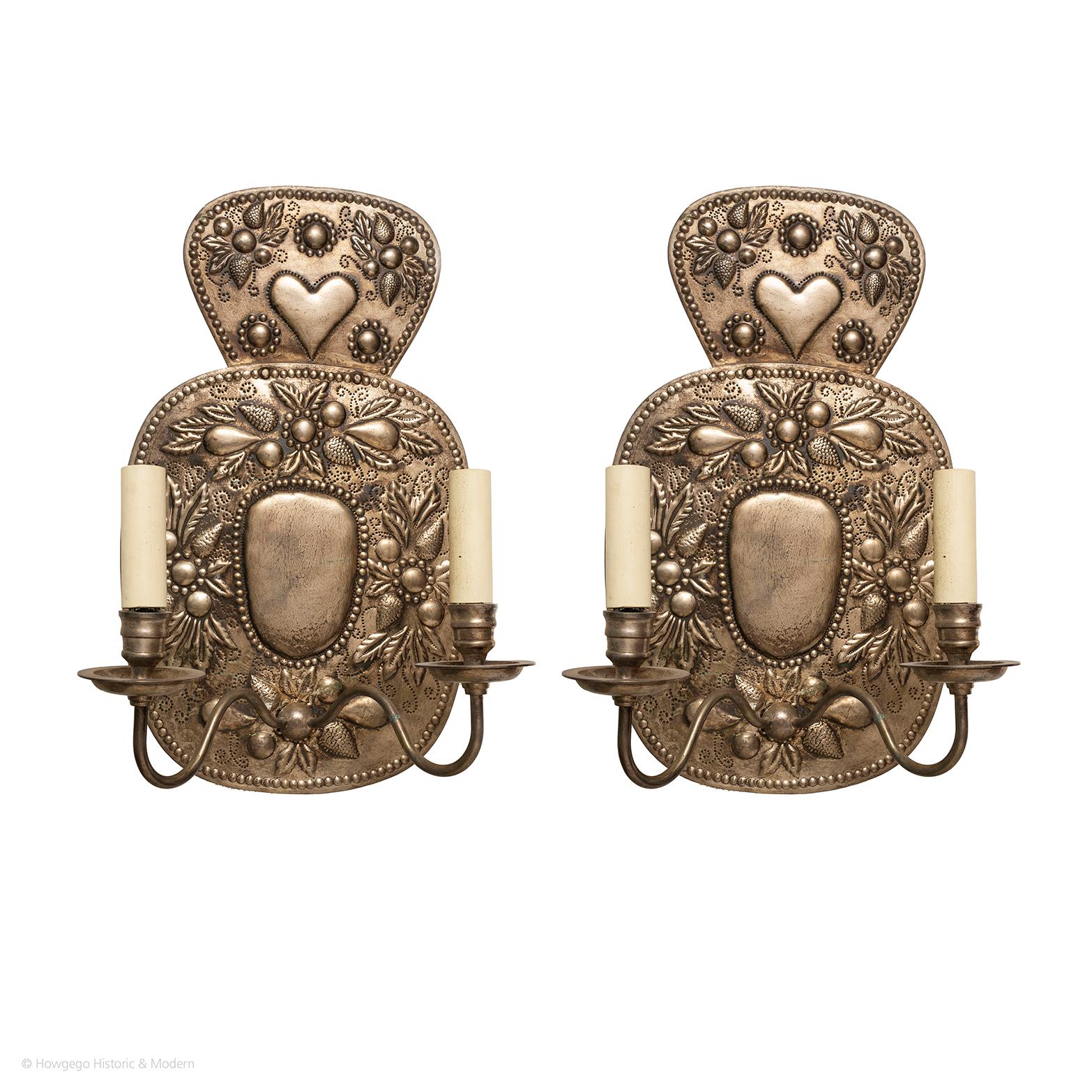 A charming pair of silvered, Repousse, wall sconces with heart motif Crestings each with two arms

- Naïve charm with the heart motifs and stylised leaves and berries
- The silvered metal maximises the reflection of light 
They blend and sit
